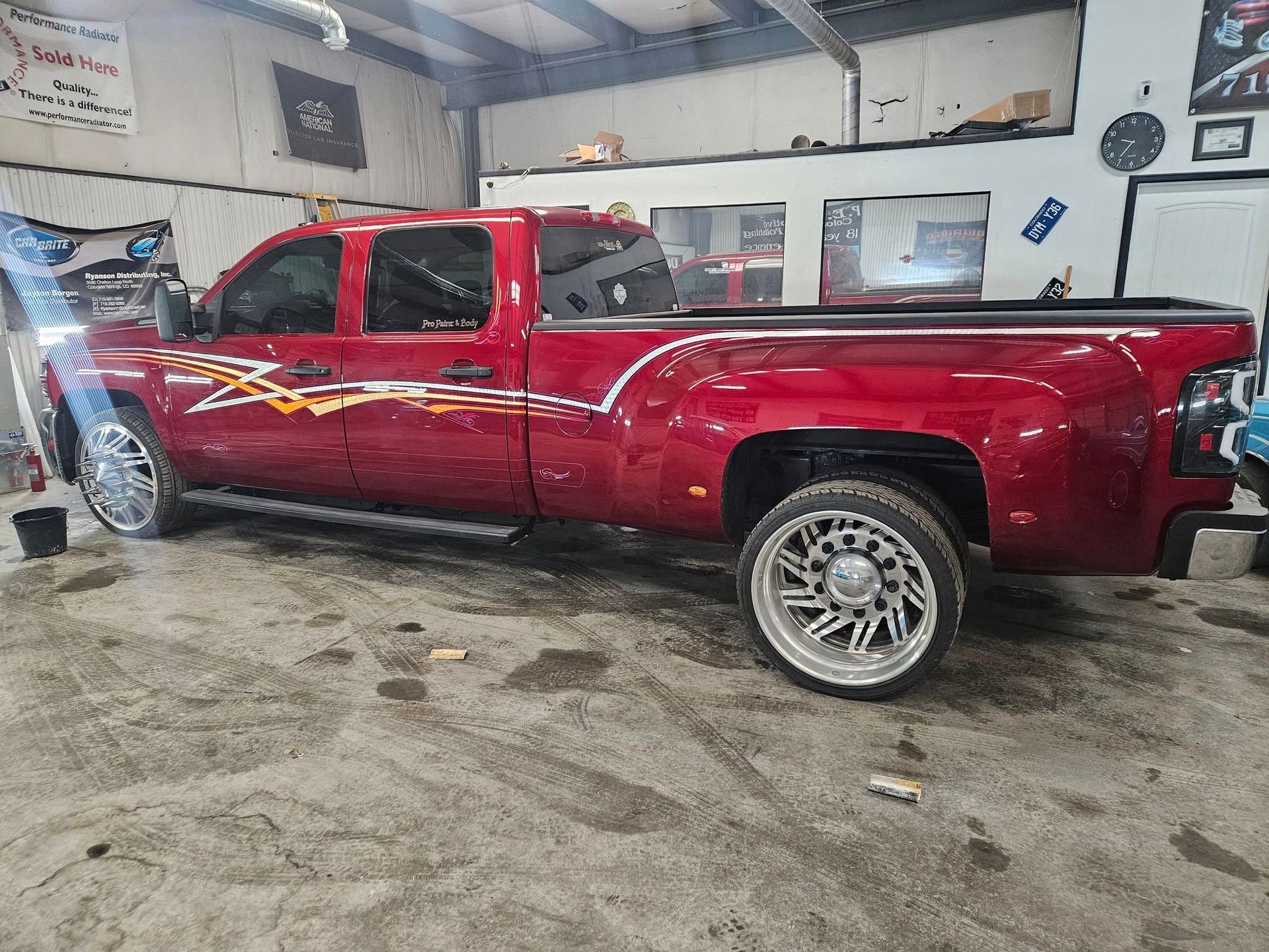Red pickup truck with custom wheels and a flame decal parked inside a garage.
