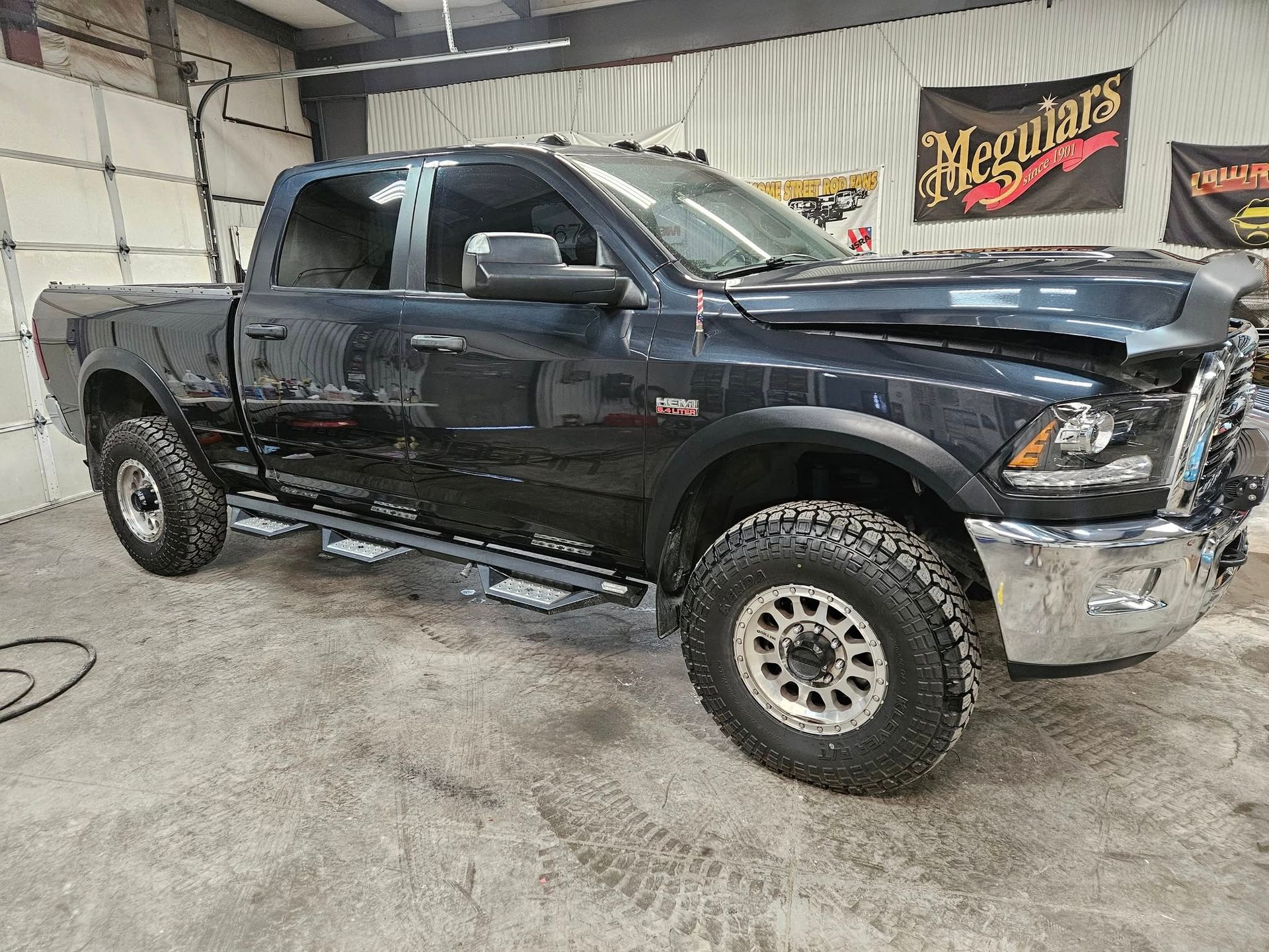 Dark blue Ram pickup truck parked inside a garage, with large tires and running boards.
