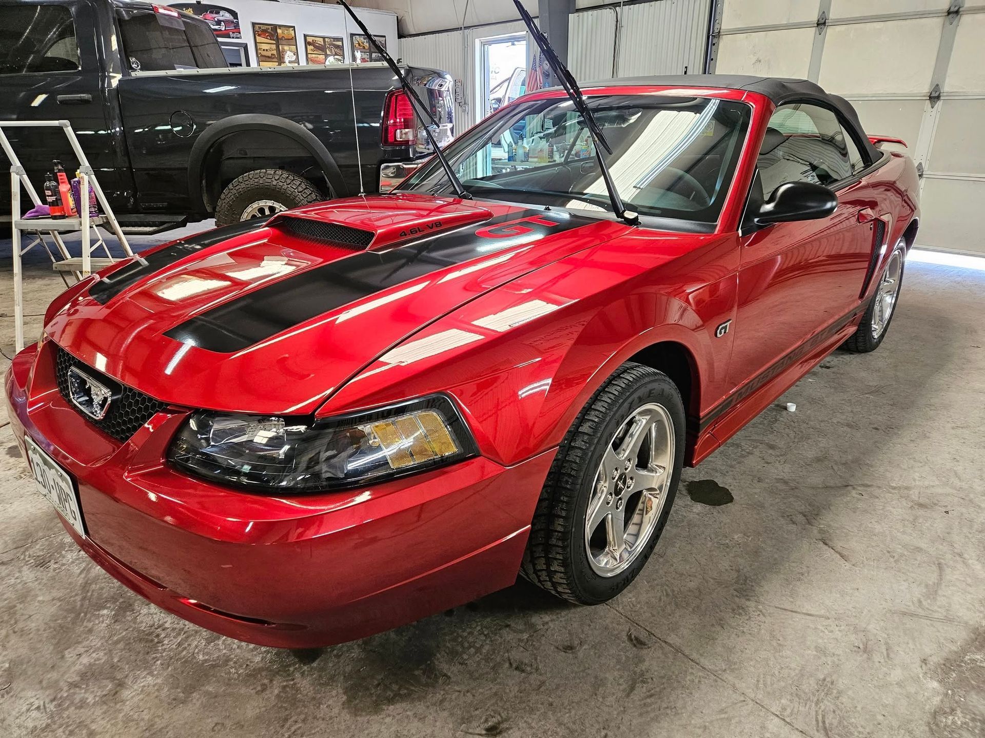 Red Ford Mustang convertible with black racing stripes in a garage.