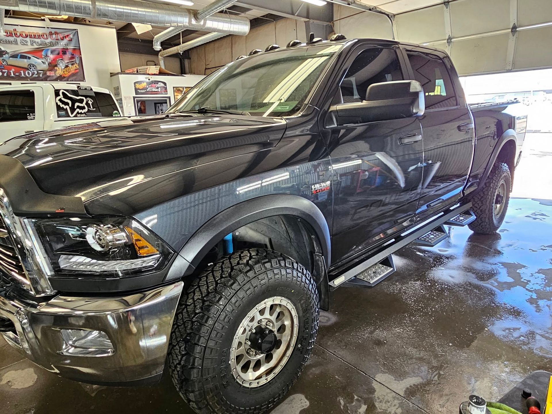 Black Dodge Ram truck parked in a garage, with large tires, and a running board.