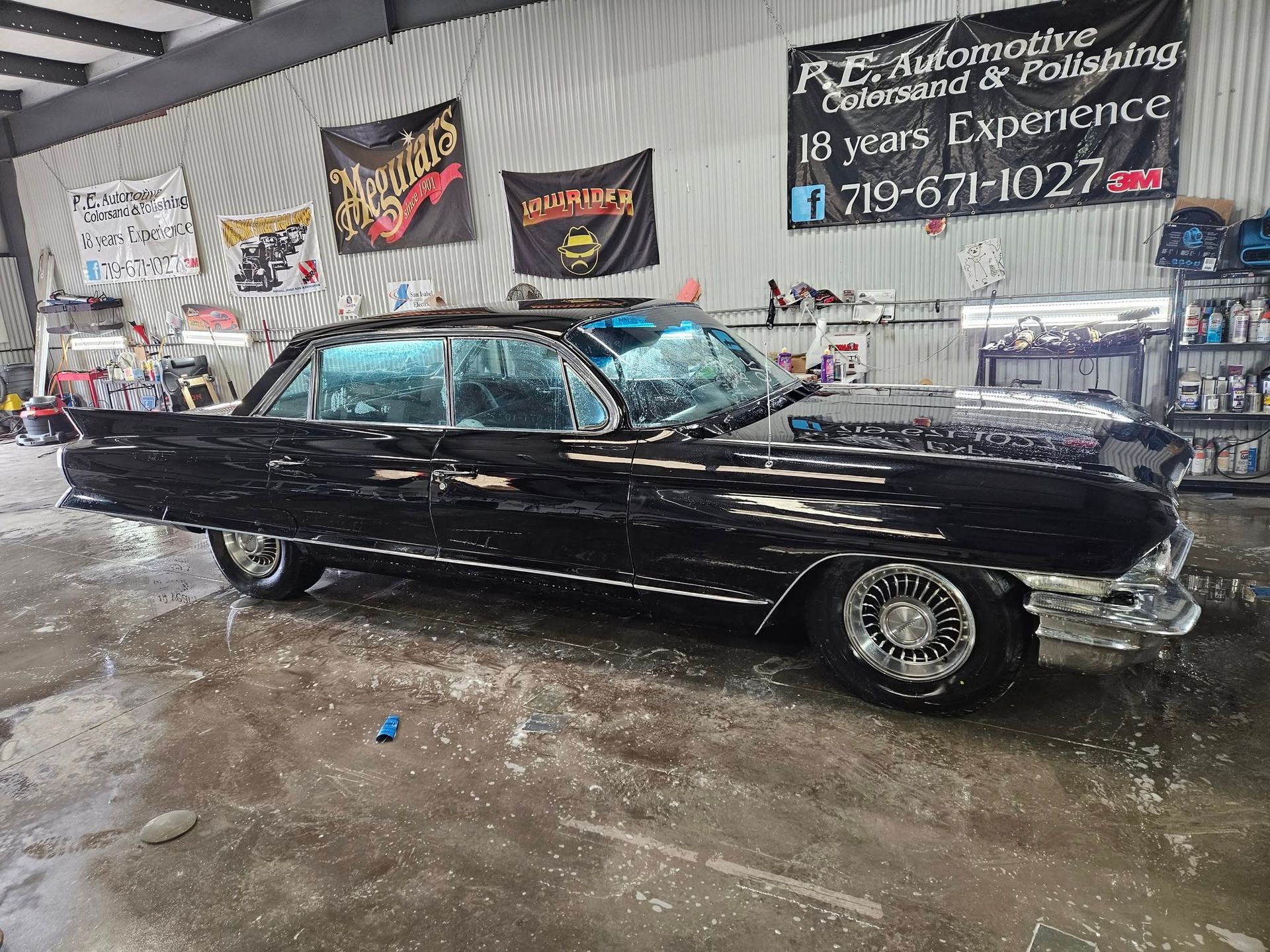 Black classic car being washed inside an automotive detailing shop.