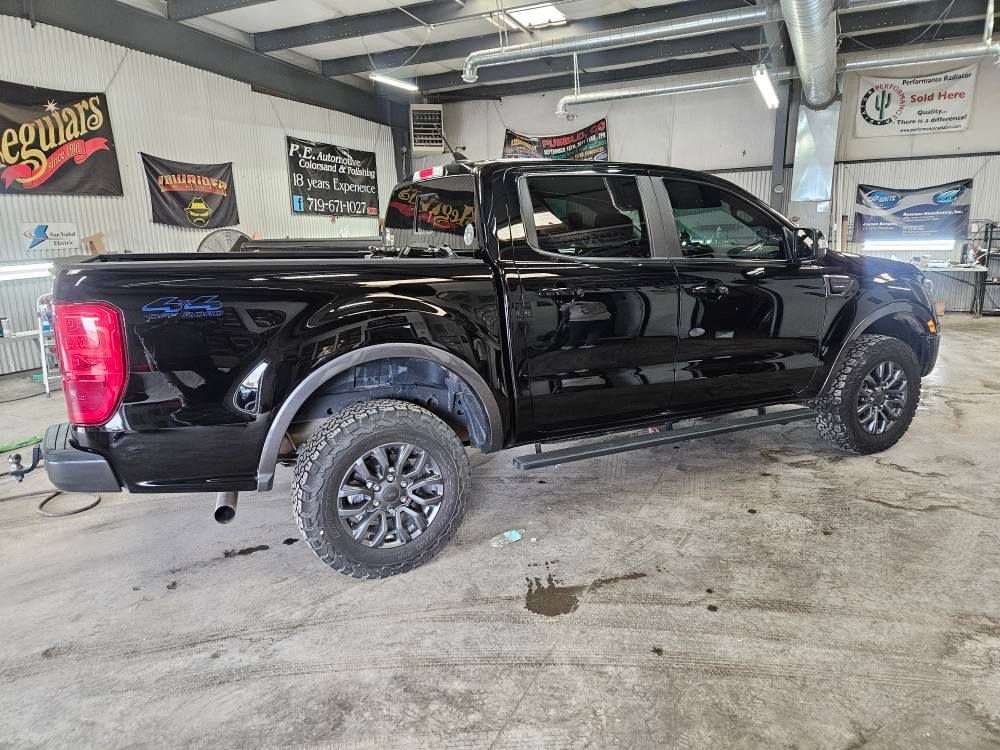 Black Ford Ranger pickup truck with black wheels and fender flares in a garage.