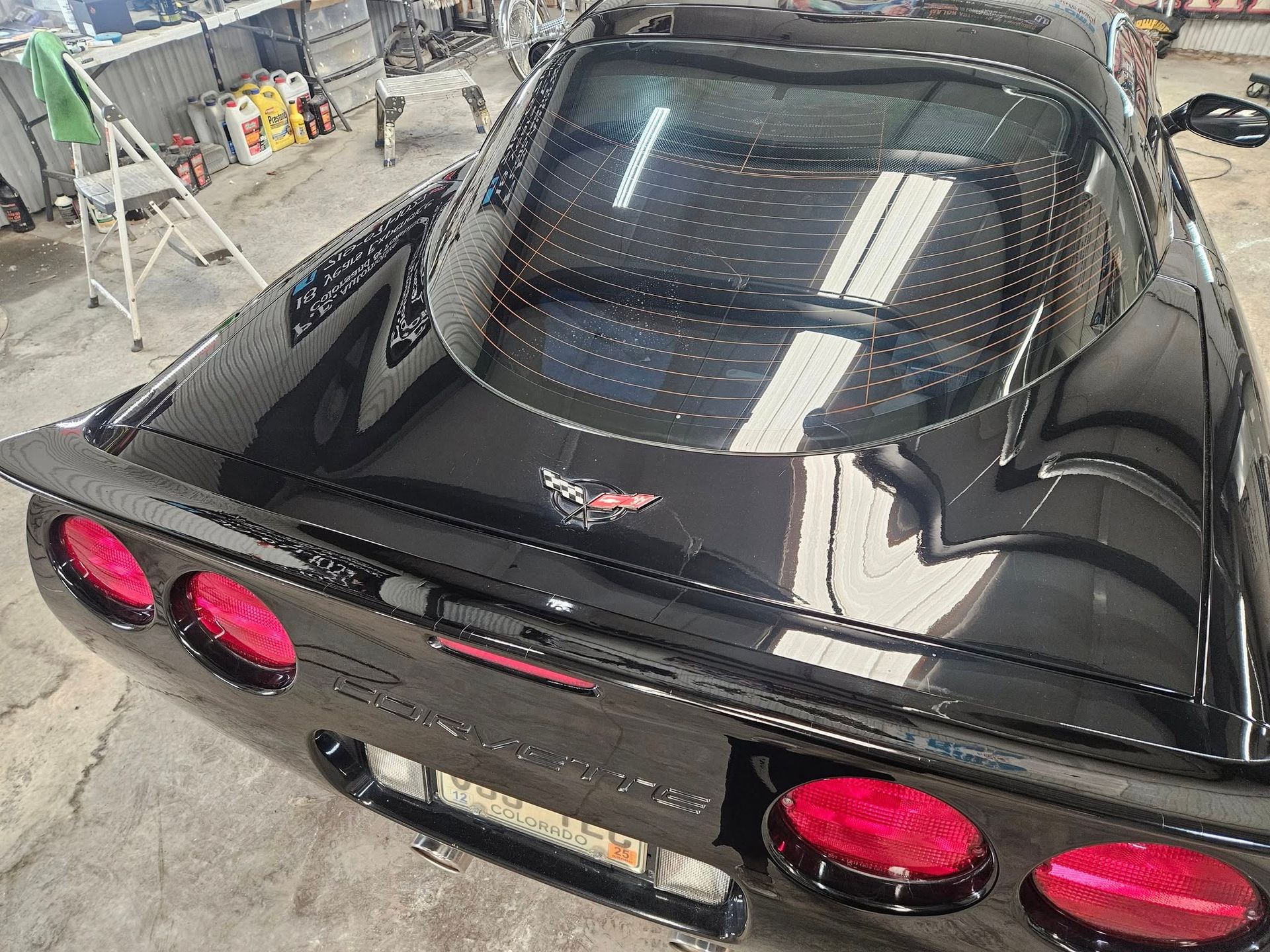 Black Corvette sports car, rear view, red tail lights, in a workshop.
