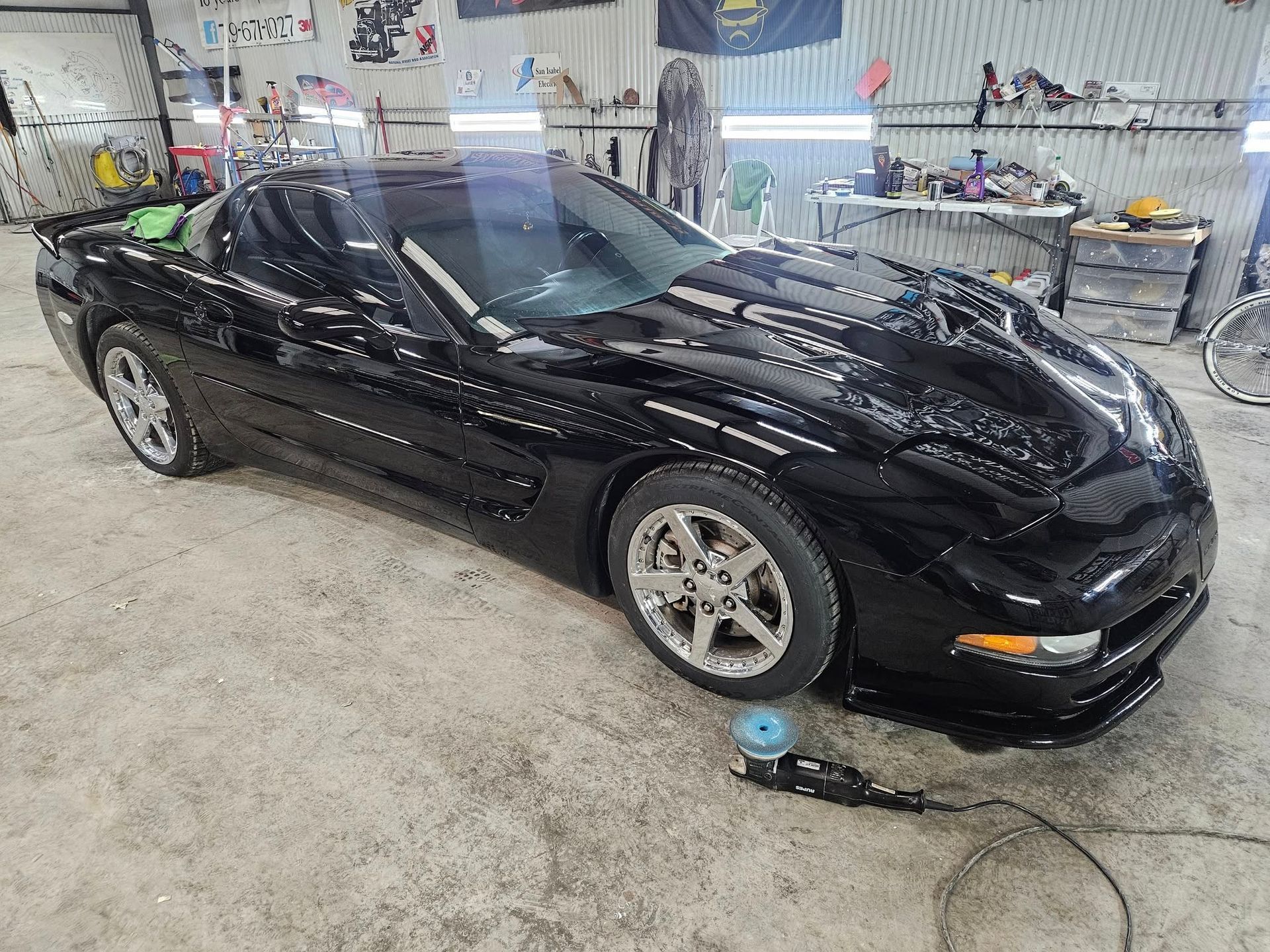 Black Corvette in a workshop, near a tool on the floor.