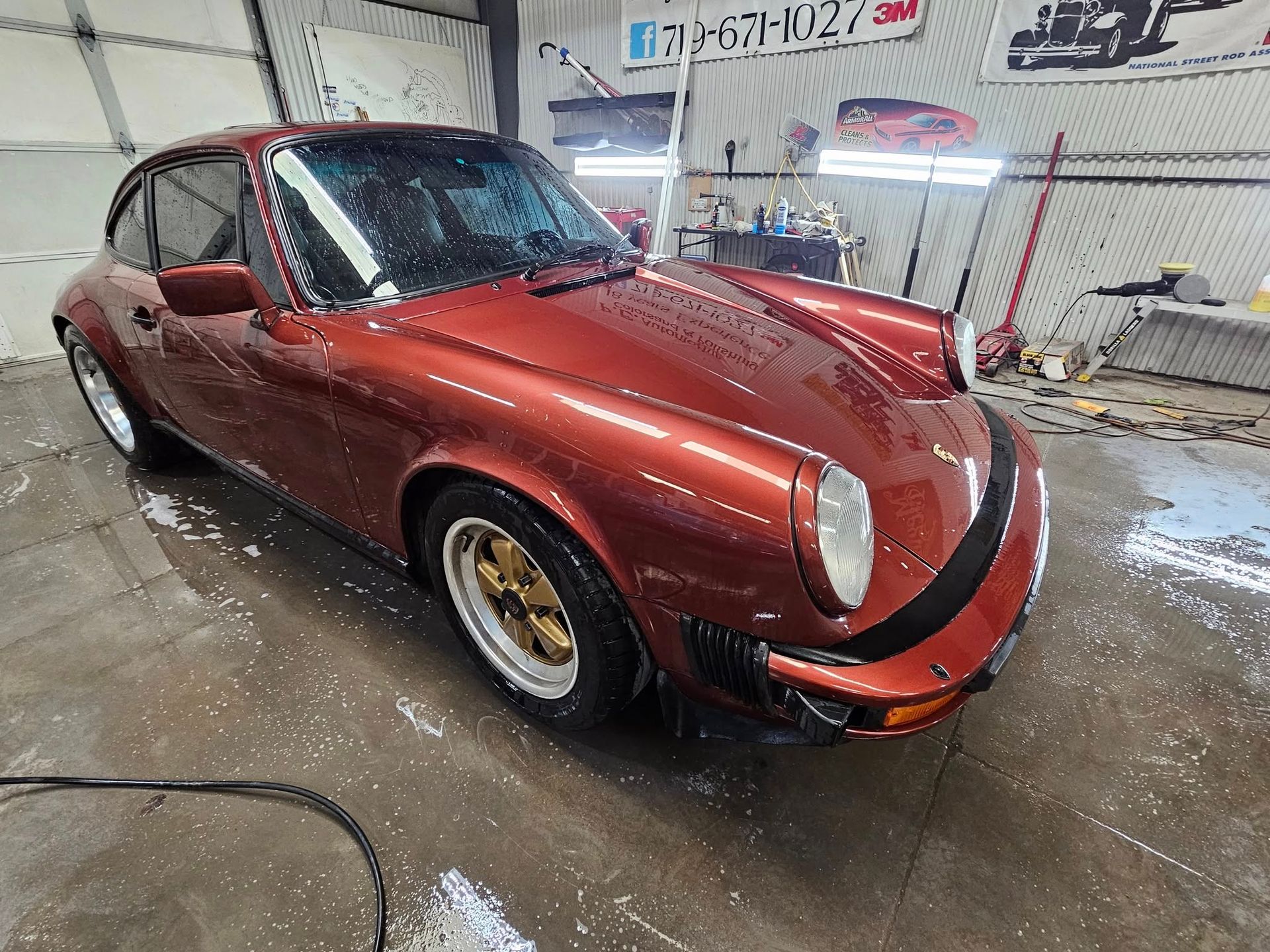 A classic red Porsche being washed in a garage, water spraying.