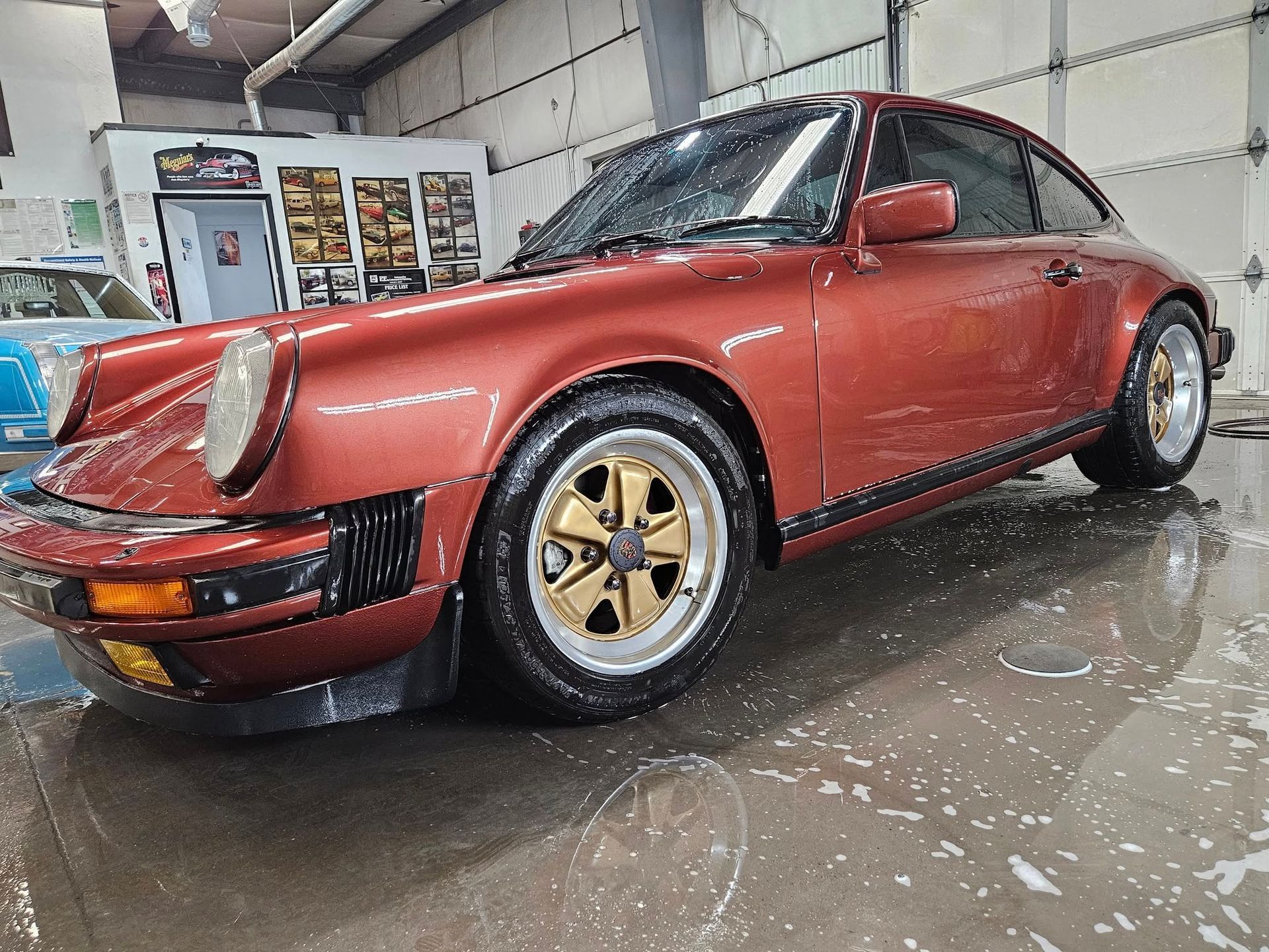 Red Porsche 911 with gold wheels, in a car wash bay.