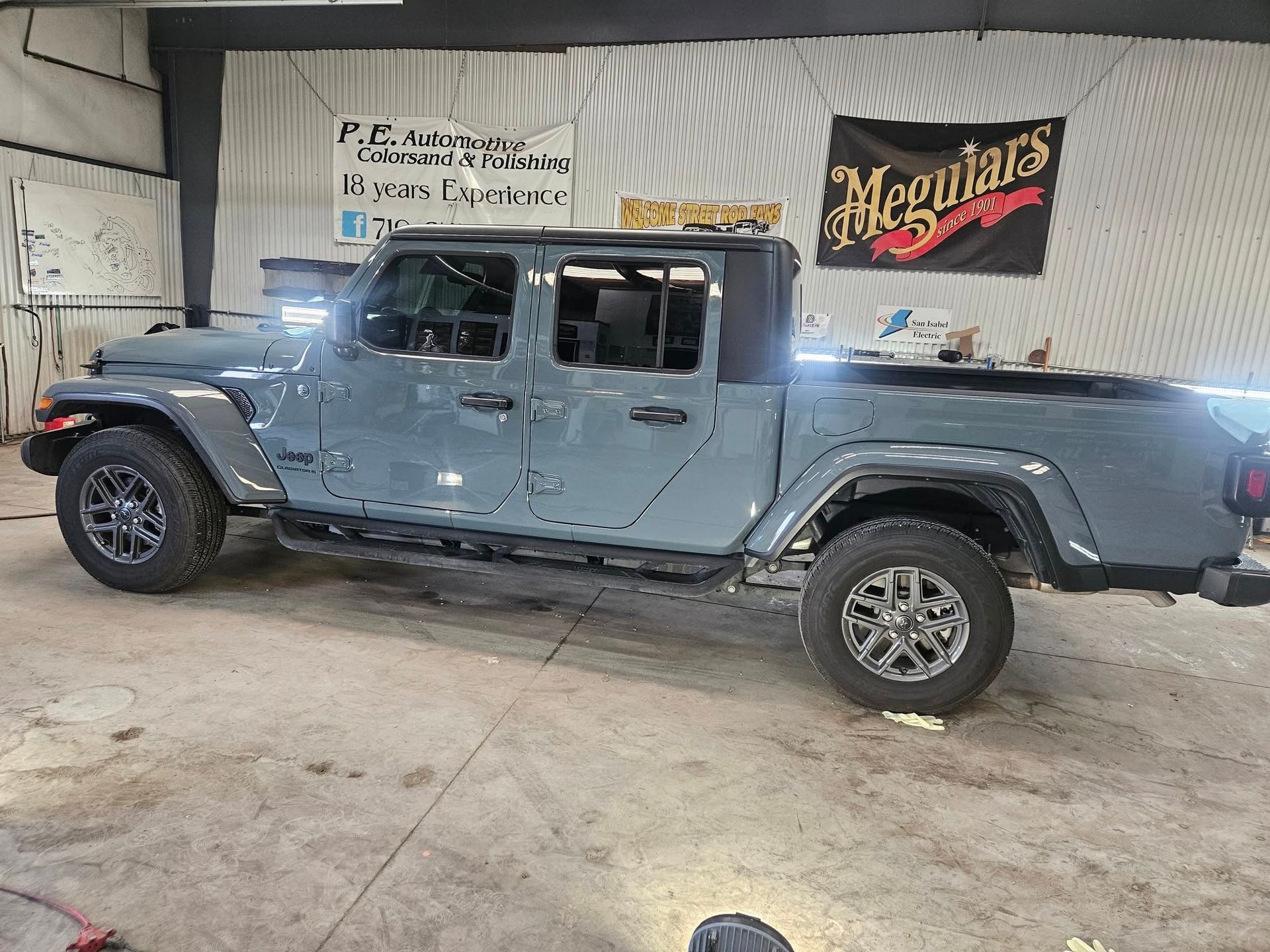 Gray Jeep Gladiator truck parked inside a garage, with Meguiar's banner in the background.