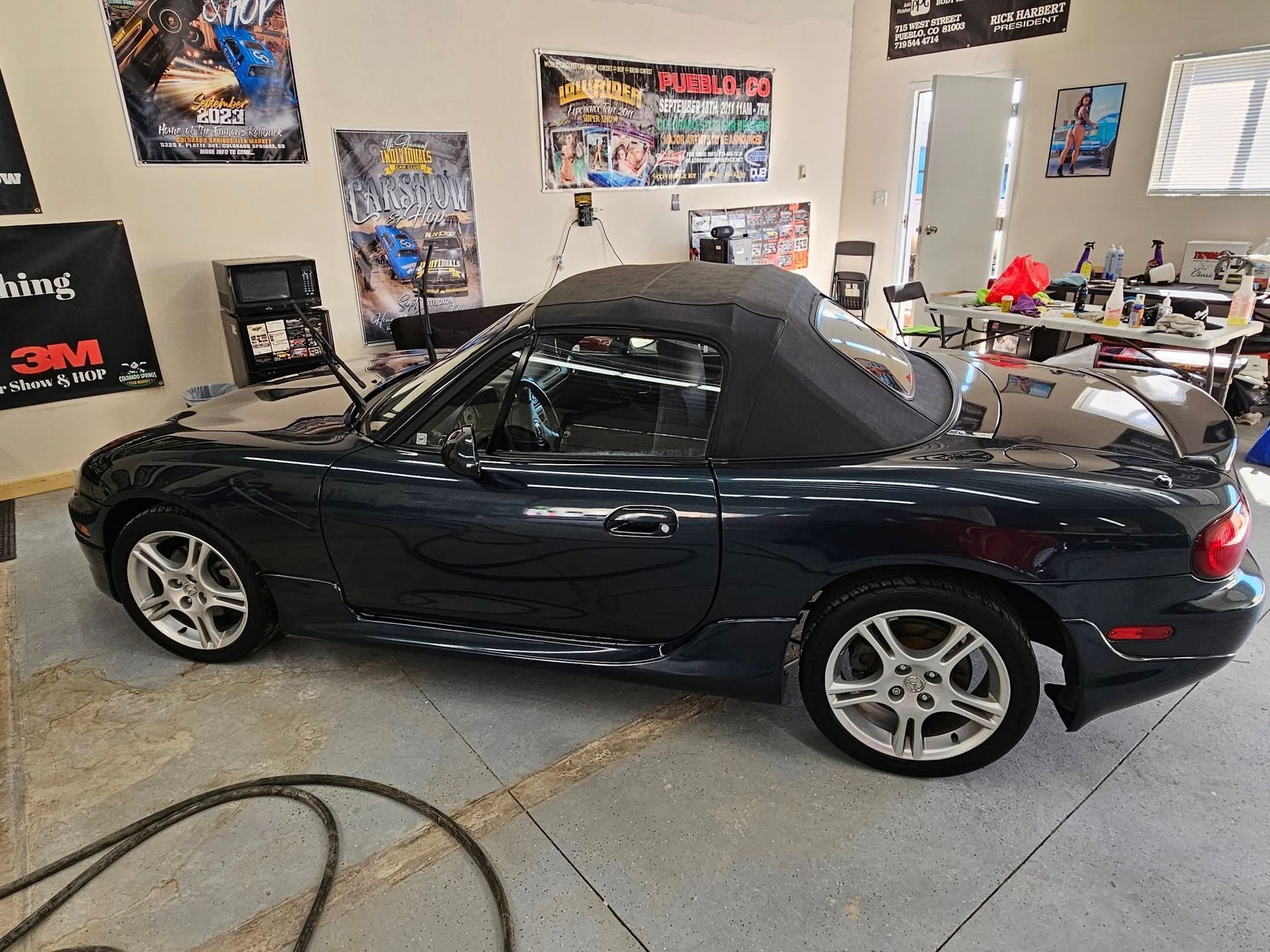 Dark blue convertible sports car inside a garage with posters on the walls.
