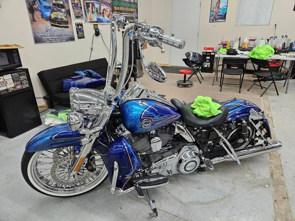 Blue and chrome custom motorcycle inside a shop with a black couch, tables, and posters.