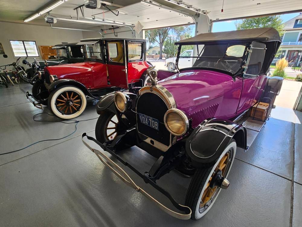 Two vintage cars, one purple, one red, parked in a garage.