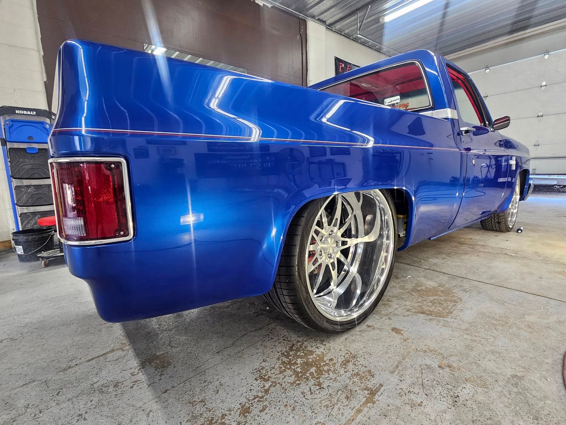 Blue custom pickup truck with chrome wheels lowered in a garage.