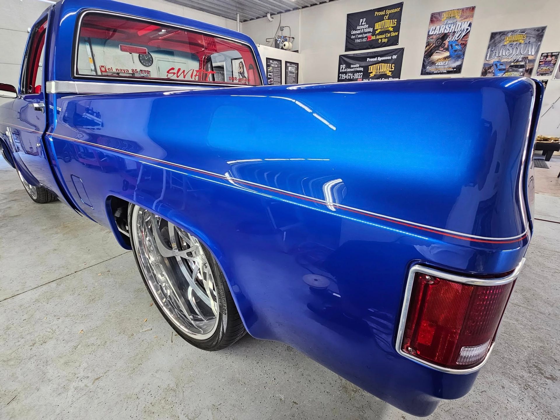 Blue custom pickup truck with chrome wheels in a shop.