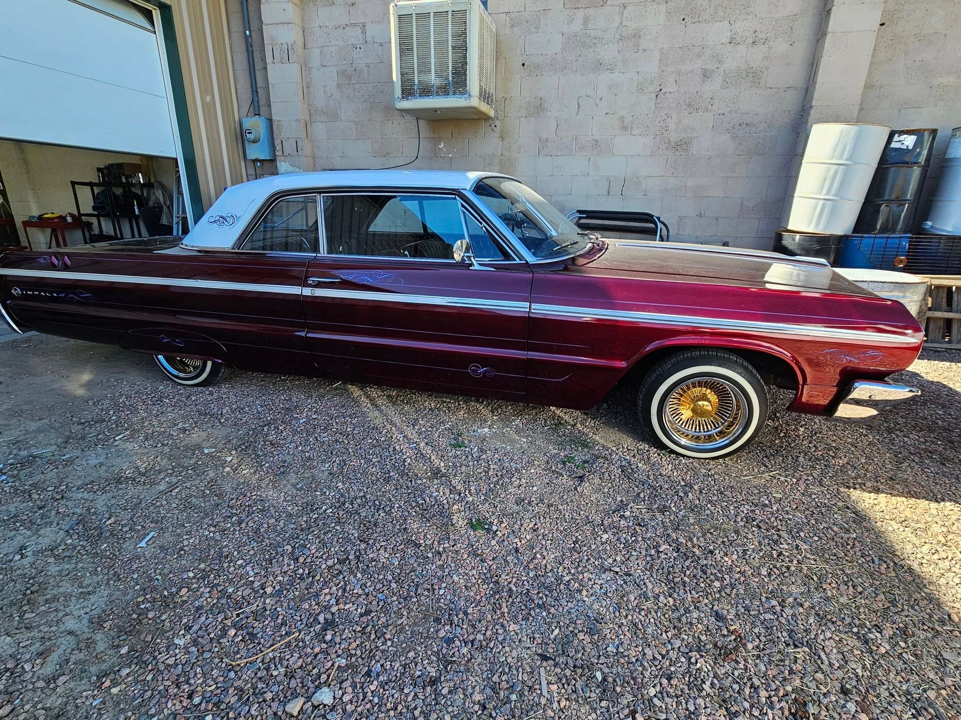 Burgundy and white lowrider car parked outside a garage.