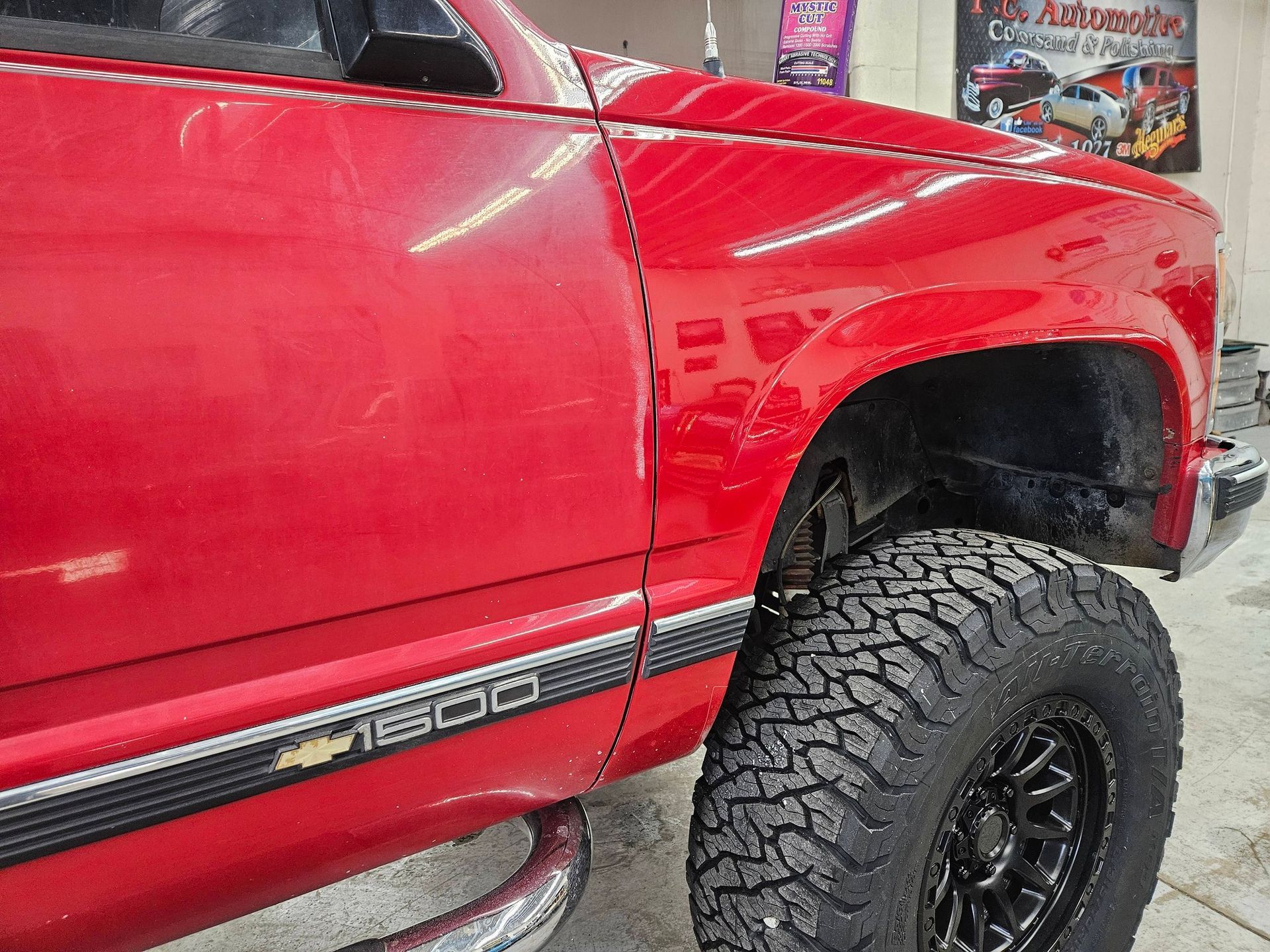 Red Chevrolet Silverado 1500 truck with large black off-road tire.