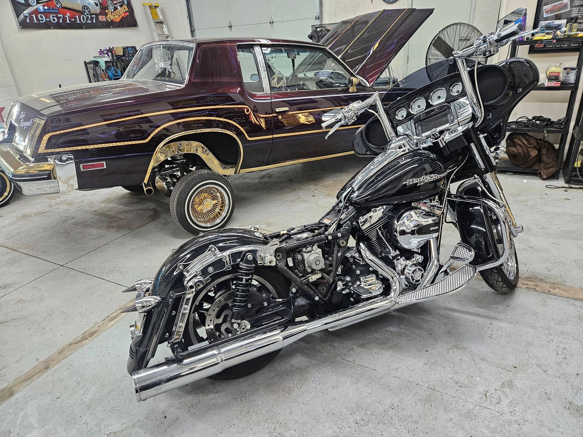 A chrome Harley-Davidson motorcycle and a maroon lowrider car in a garage.