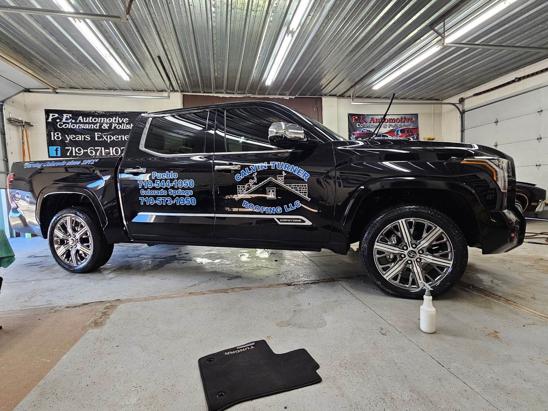 Black pickup truck with chrome wheels inside a garage.
