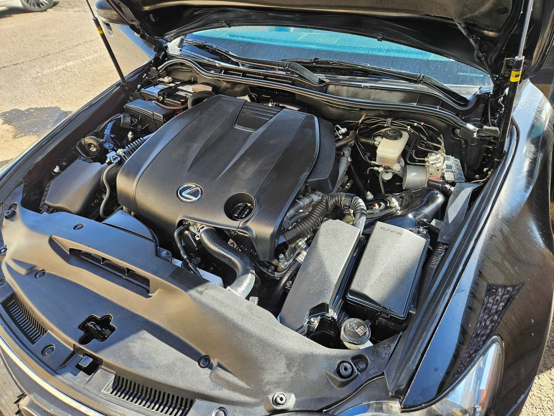 Black car engine with hood open, showing the engine components and the engine cover, in daylight.