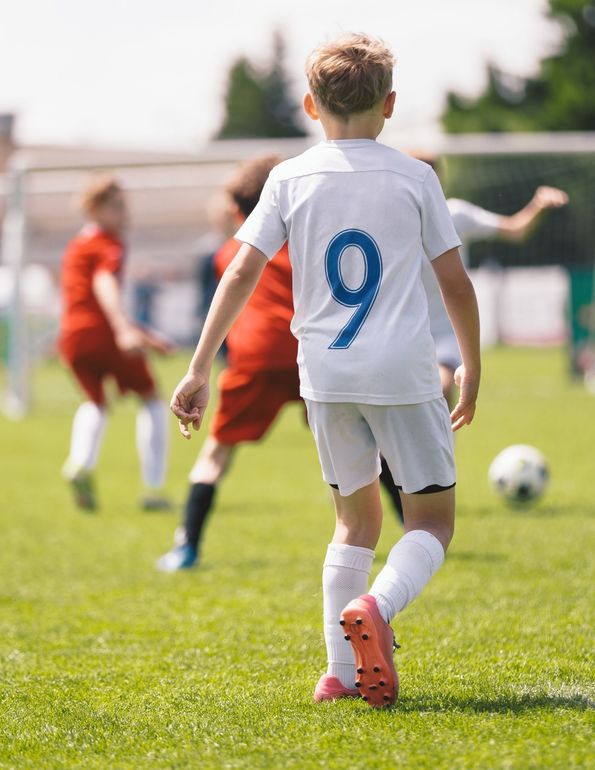 A soccer player in a white uniform with number 9 on the back stands on a field during a game with other players nearby.