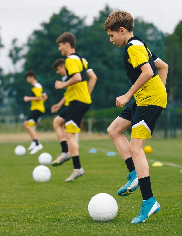 Soccer players in yellow and black uniforms practice footwork drills with soccer balls on a grass field.