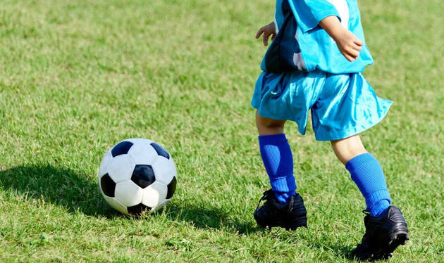 A person in a blue soccer uniform dribbling a soccer ball on a green grass field.
