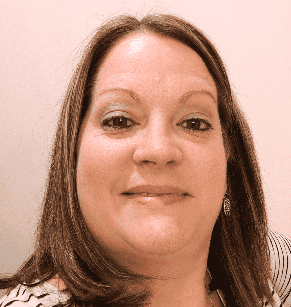 A headshot of a smiling person with shoulder-length brown hair, wearing a patterned top against a light background.