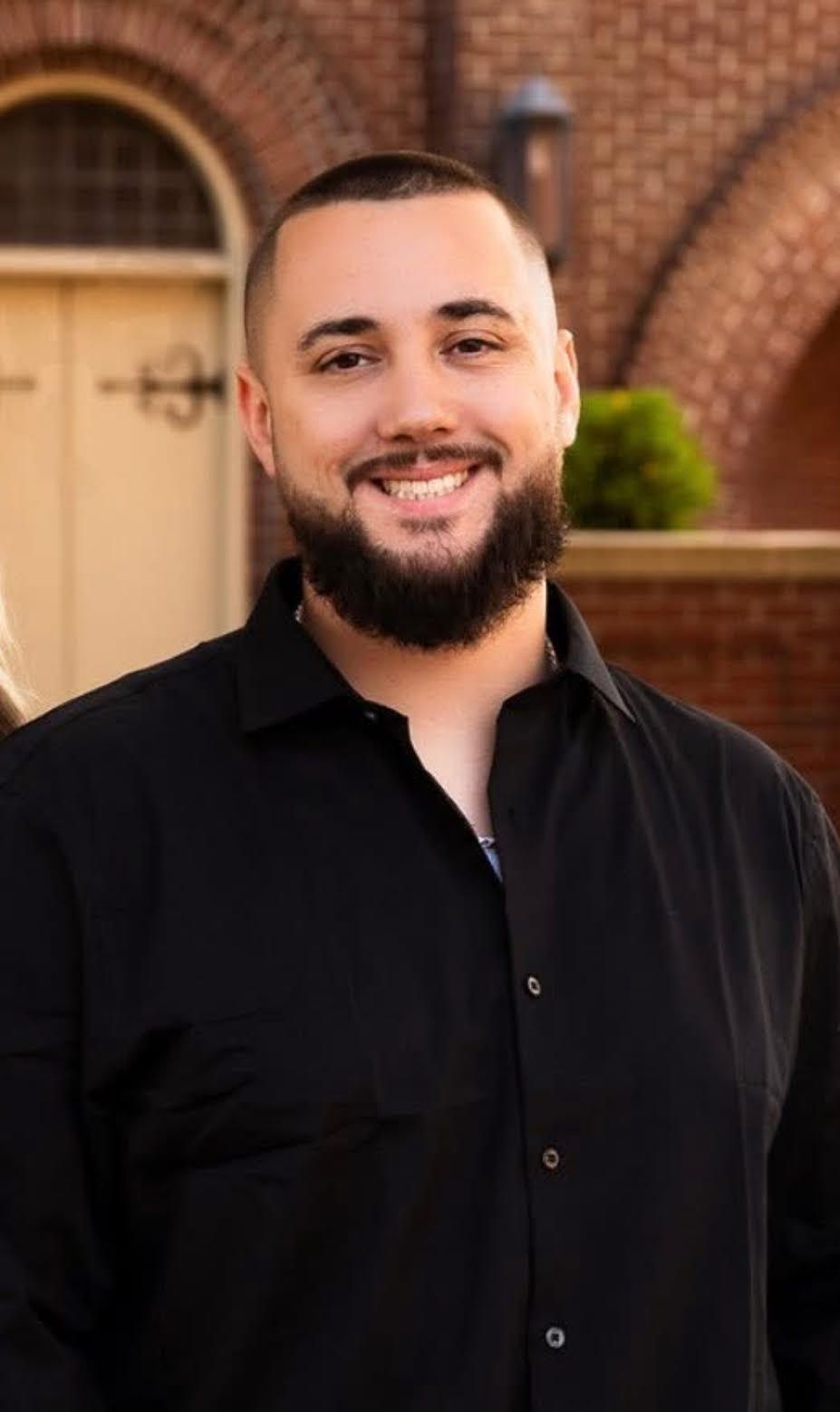 Man in green polo stands on a football field, arms crossed, stadium in background.