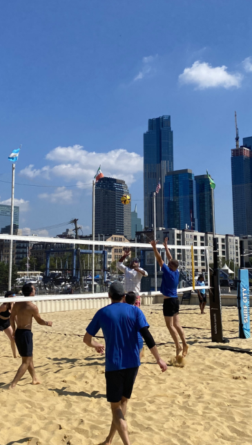 A person wearing a hat and orange shirt, holding a baseball bat on their shoulder on a baseball field.