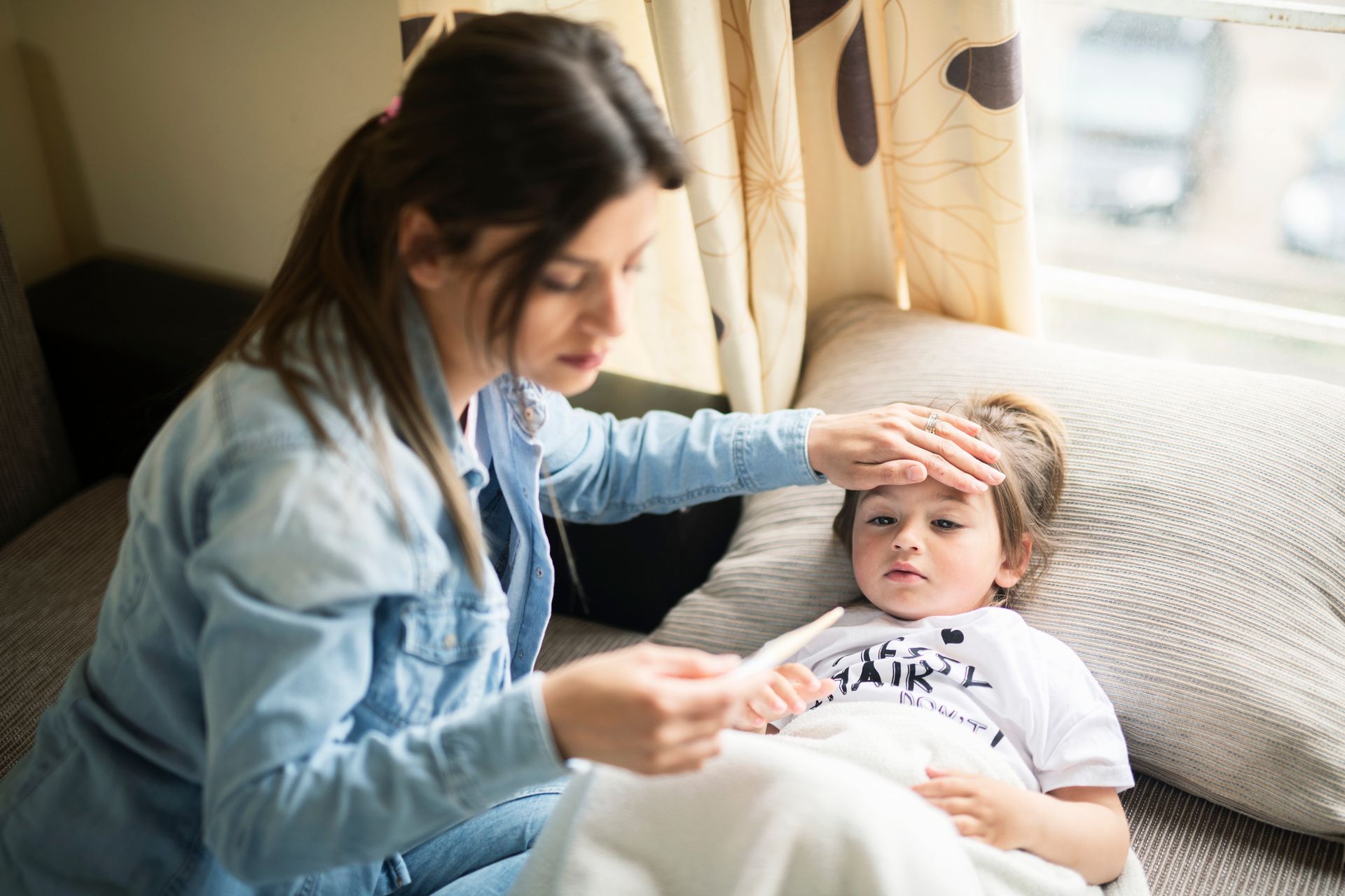 A woman is taking the temperature of a sick child.
