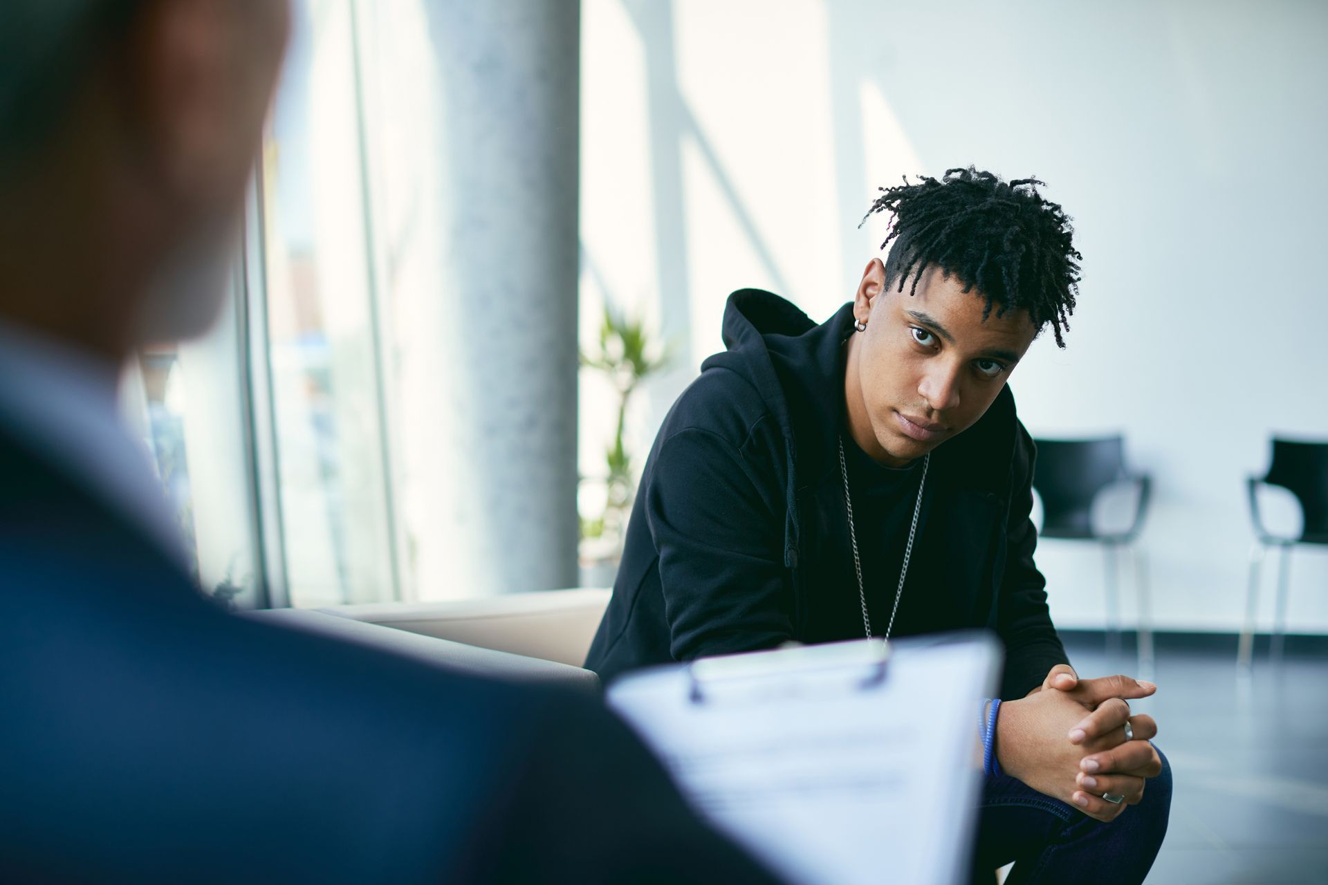 A young boy is sitting on a yellow couch talking to a woman.