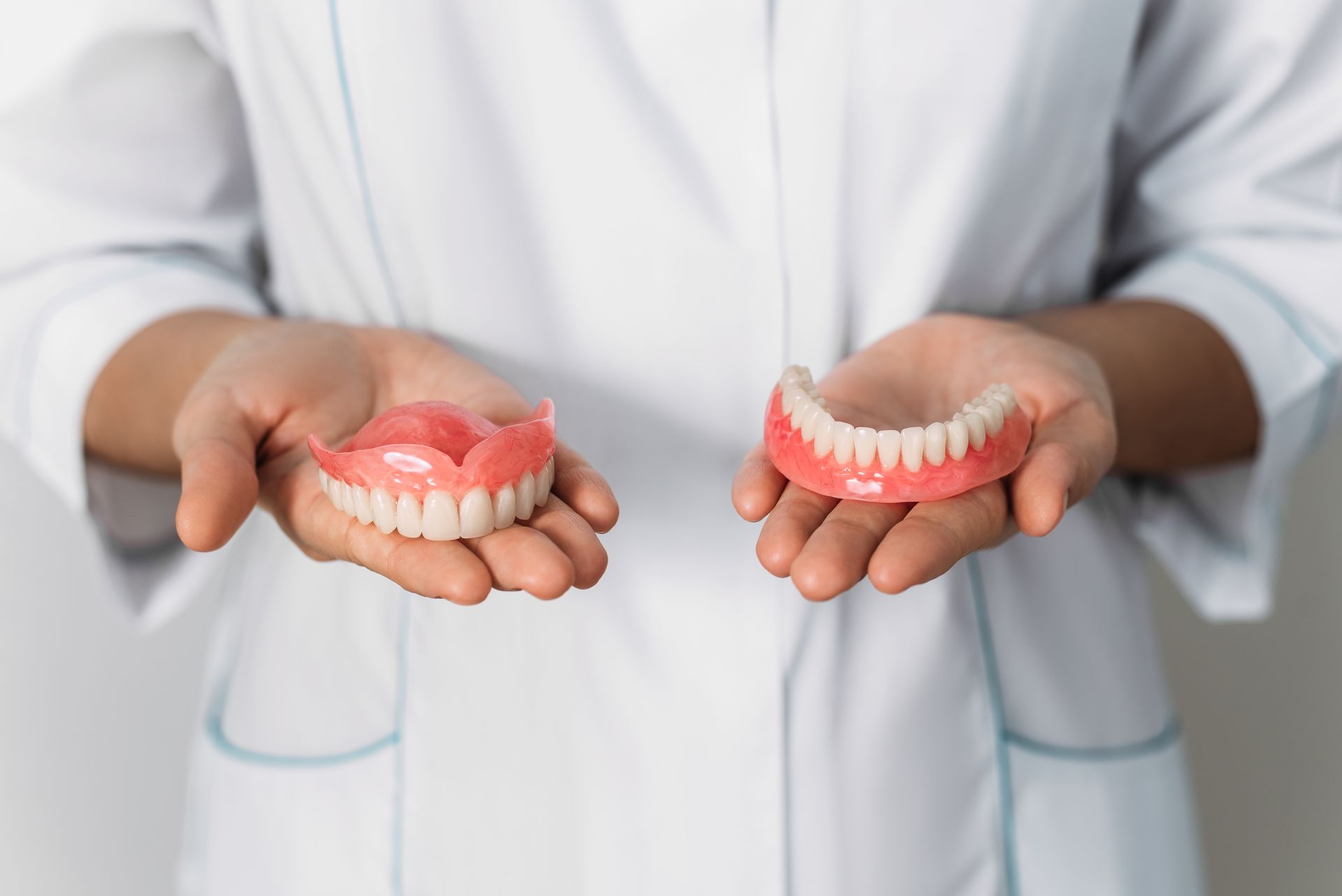 A dentist is holding two dentures in her hands.