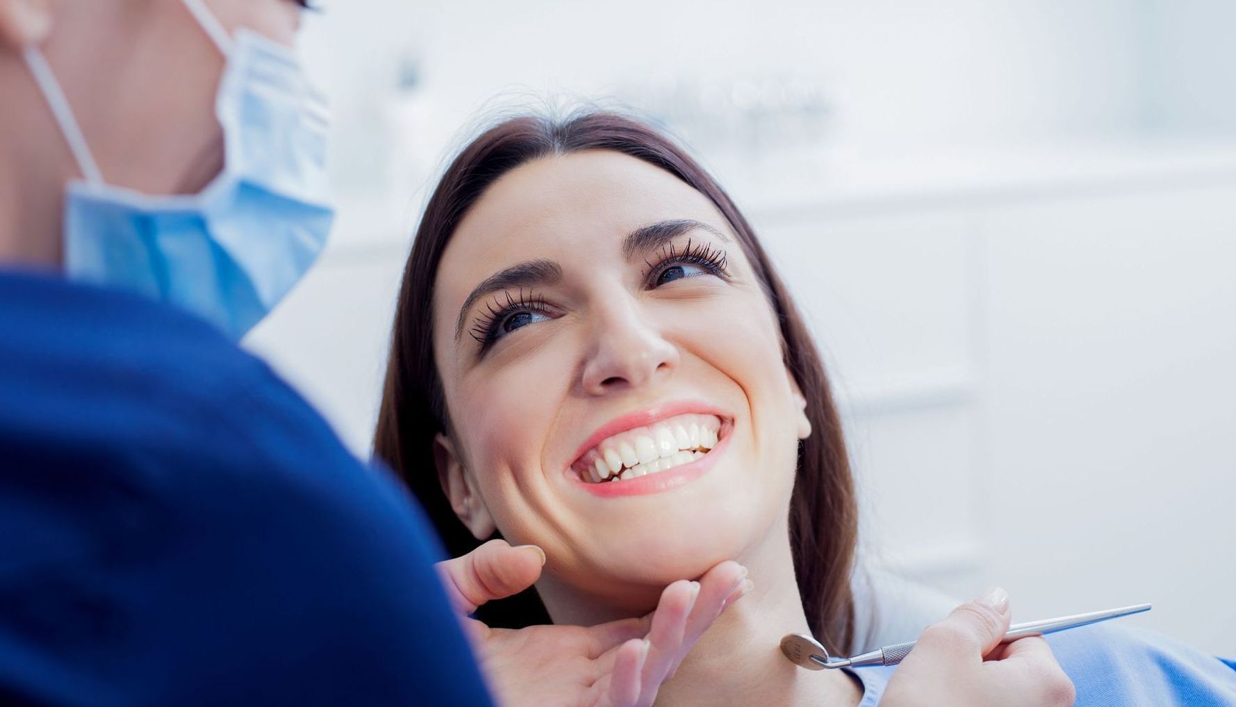 A woman is smiling while having her teeth examined by a dentist.