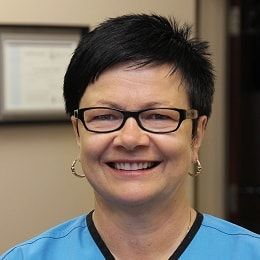 A woman wearing glasses and earrings is smiling for the camera.