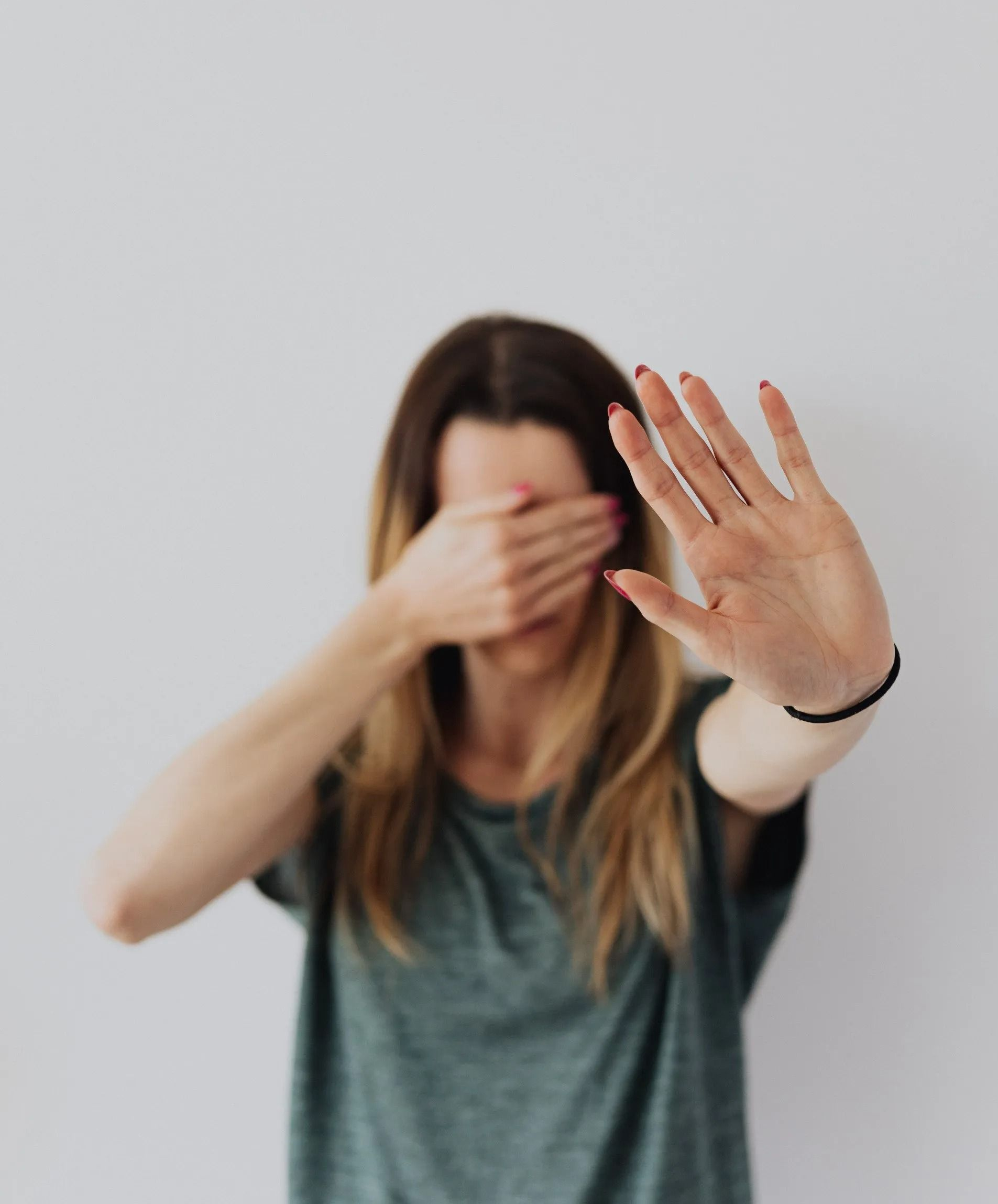 A person in a gray shirt covers their eyes with one hand and holds the other hand out in a stop gesture.