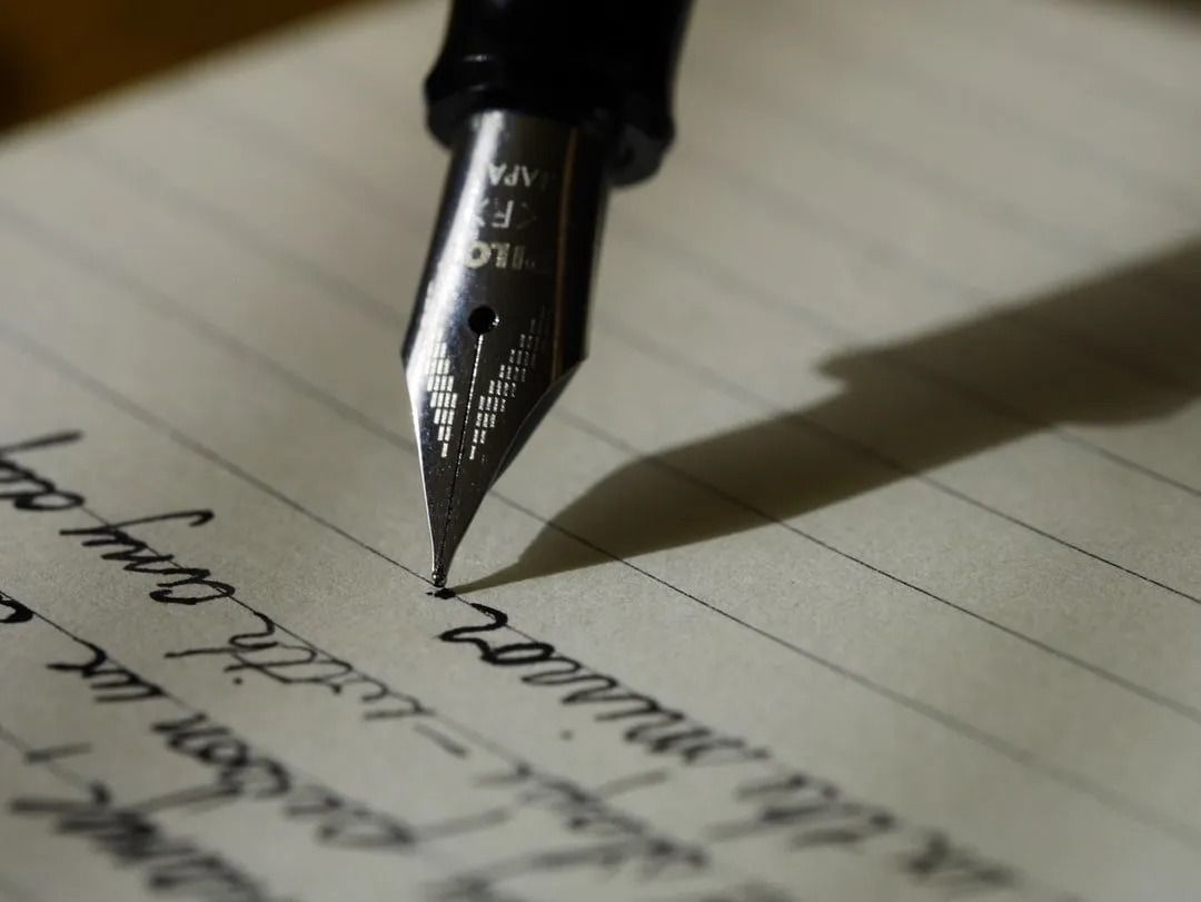 A close-up of a fountain pen nib writing cursive script on lined paper.