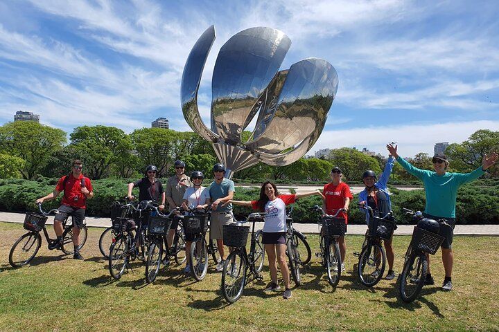 Un grupo de personas están paradas una al lado de la otra en bicicleta frente a una escultura.