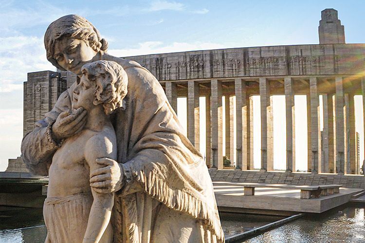 Una estatua de una mujer sosteniendo a un niño frente a un edificio.