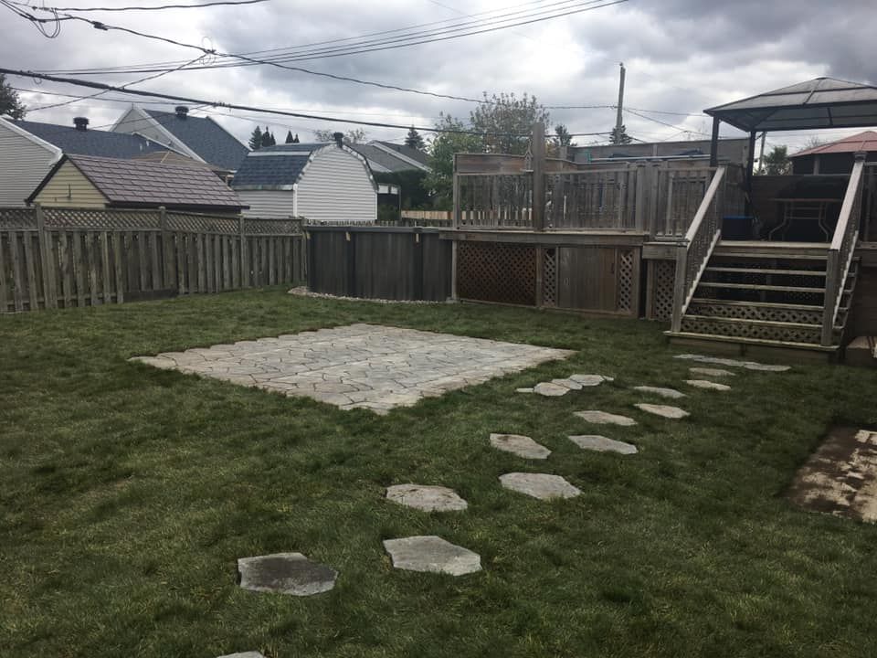 Une cour arrière avec une passerelle en pierre menant à une terrasse et des escaliers.