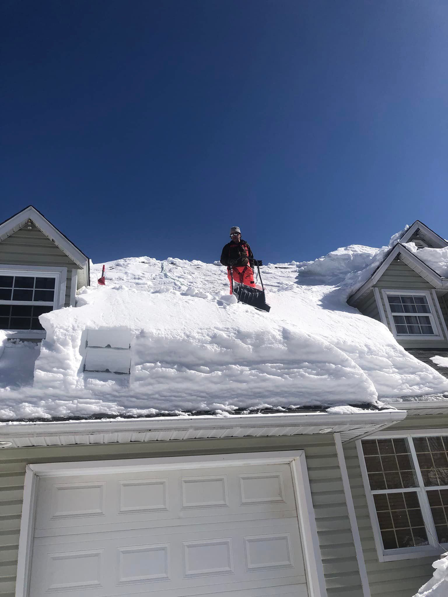 Une personne pellete la neige du toit d'une maison.