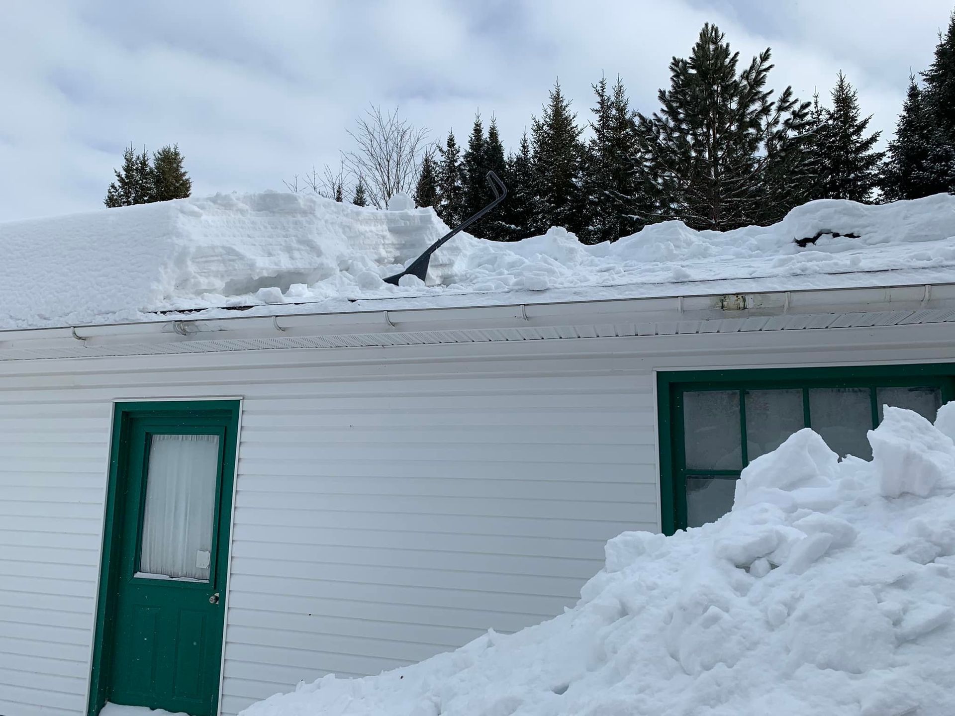 Une maison blanche avec une porte verte est couverte de neige