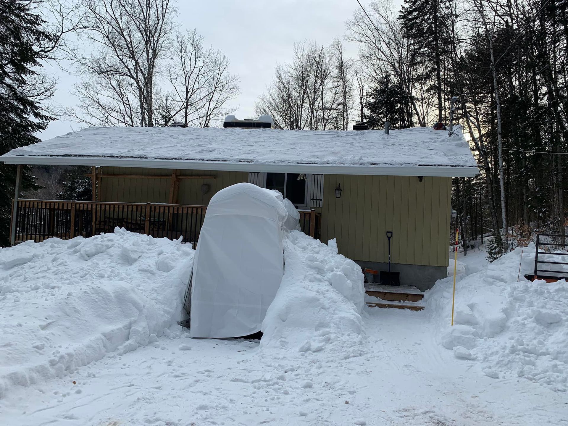 Une maison est couverte de neige et il y a un gros tas de neige devant elle