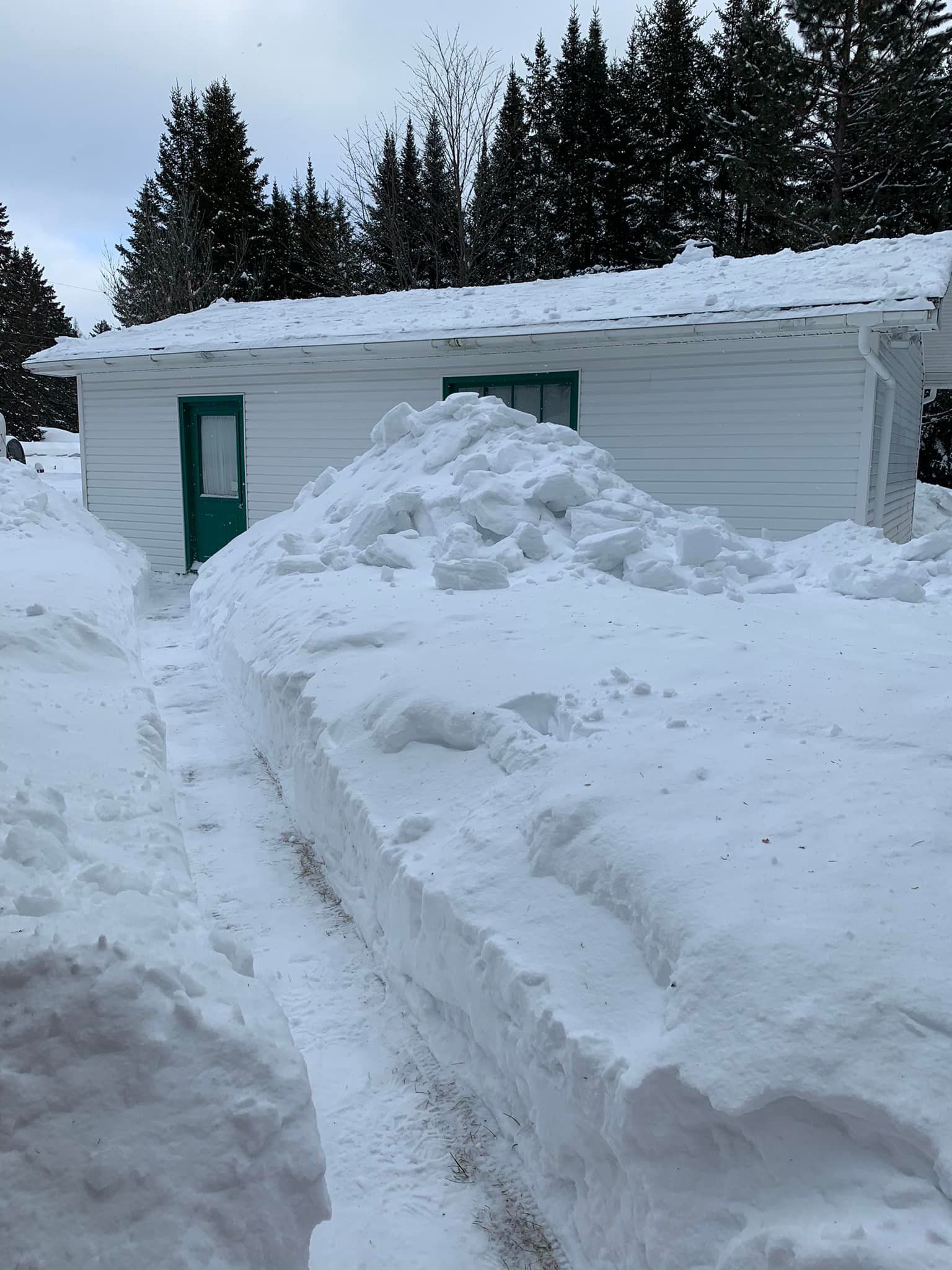 Une maison blanche avec une porte verte est couverte de neige