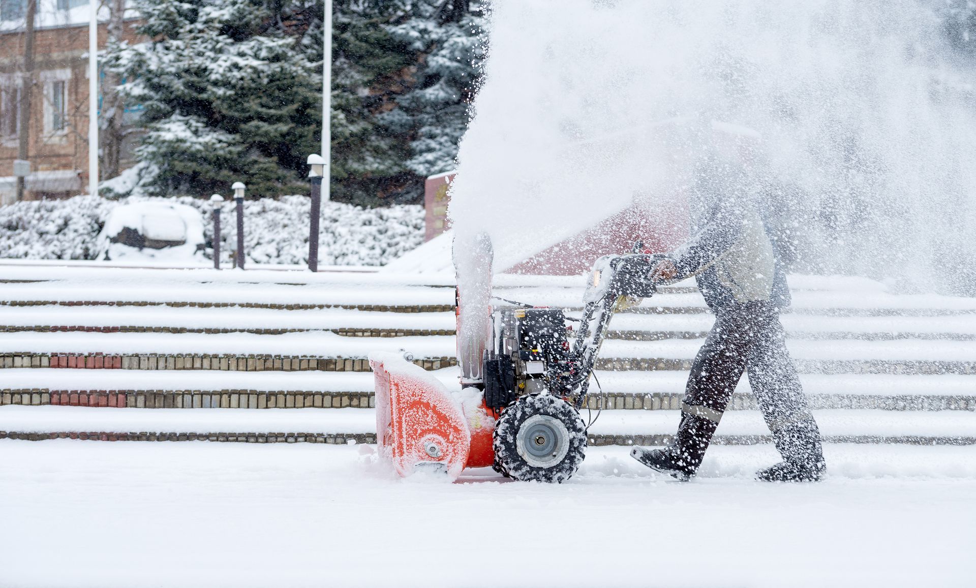 Un homme pousse une souffleuse à neige sur un trottoir enneigé.