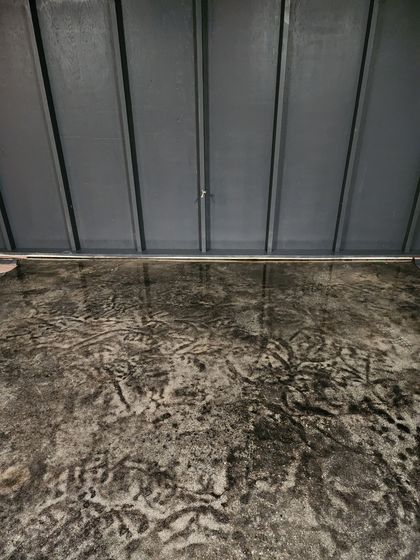 Shiny, grey epoxy floor reflecting light from windows and door, indoors. Green tape at baseboards.