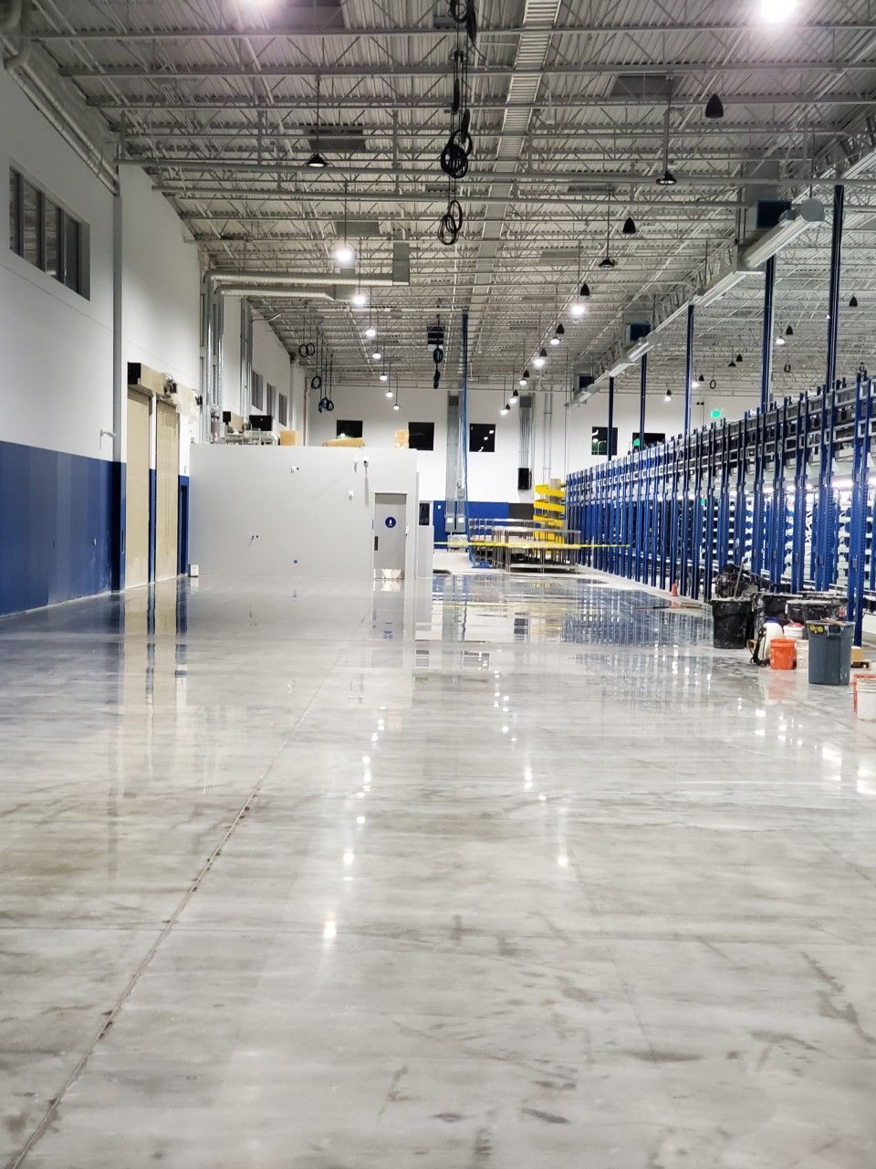 Large, empty warehouse interior with polished concrete floor, blue accents, and overhead lighting.