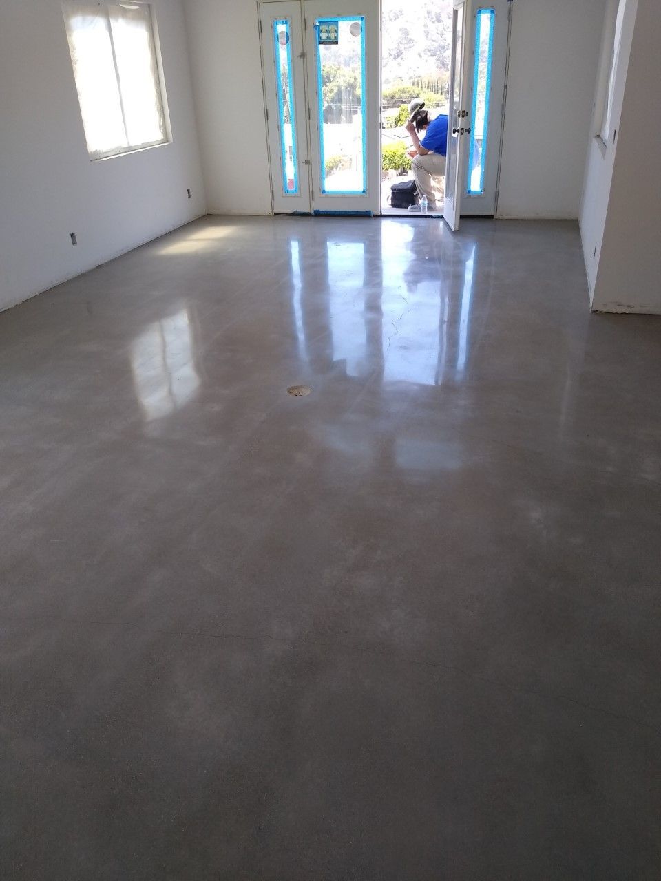 Polished concrete floor in an empty room, reflecting light. A person works near the doorway.