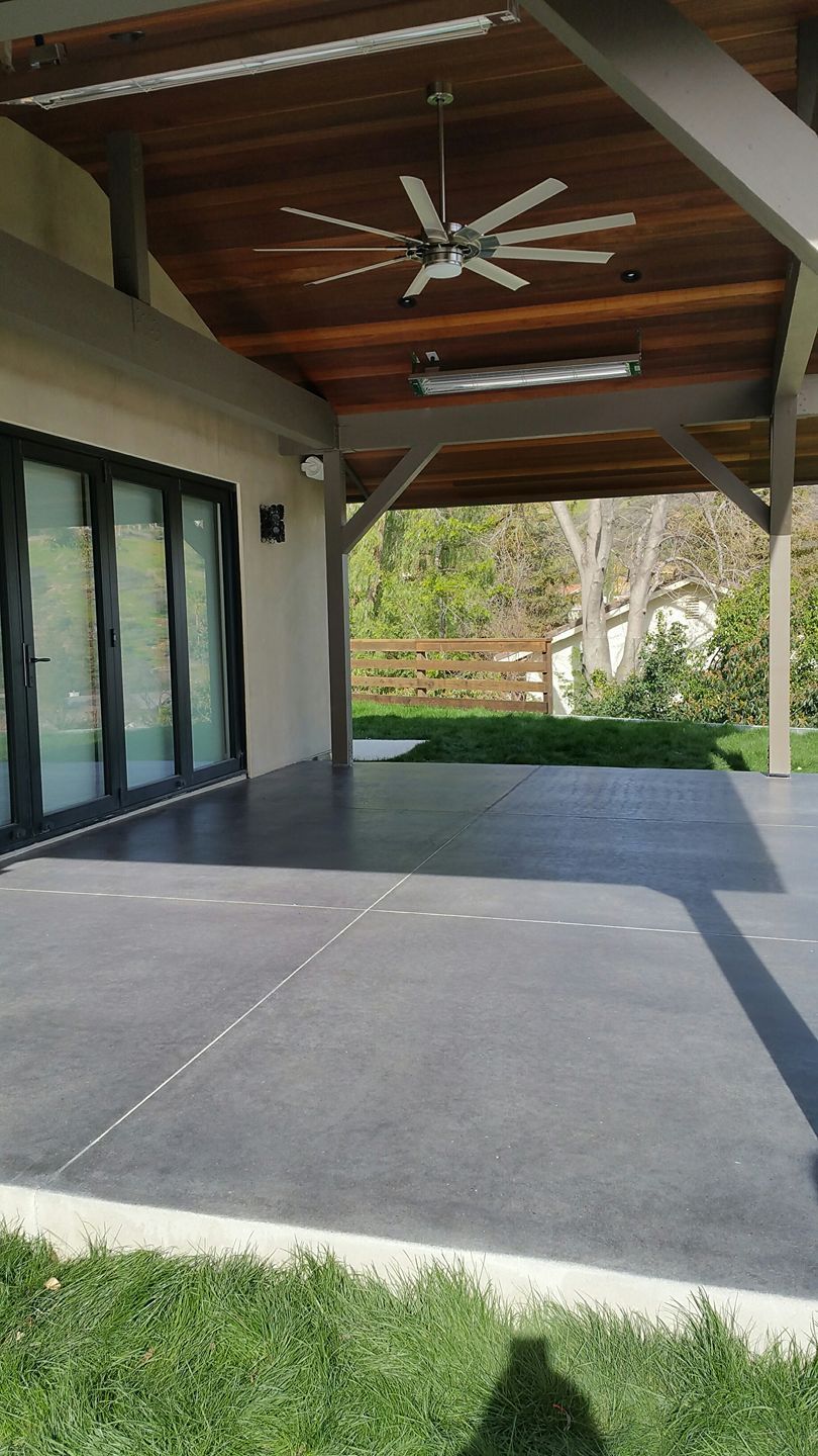 Covered patio with a dark gray concrete floor, wooden ceiling, and sliding glass doors.