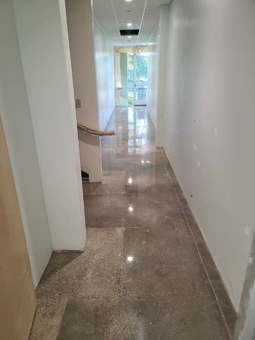Narrow hallway with polished concrete floor, white walls, and a door at the end leading to an outside area.