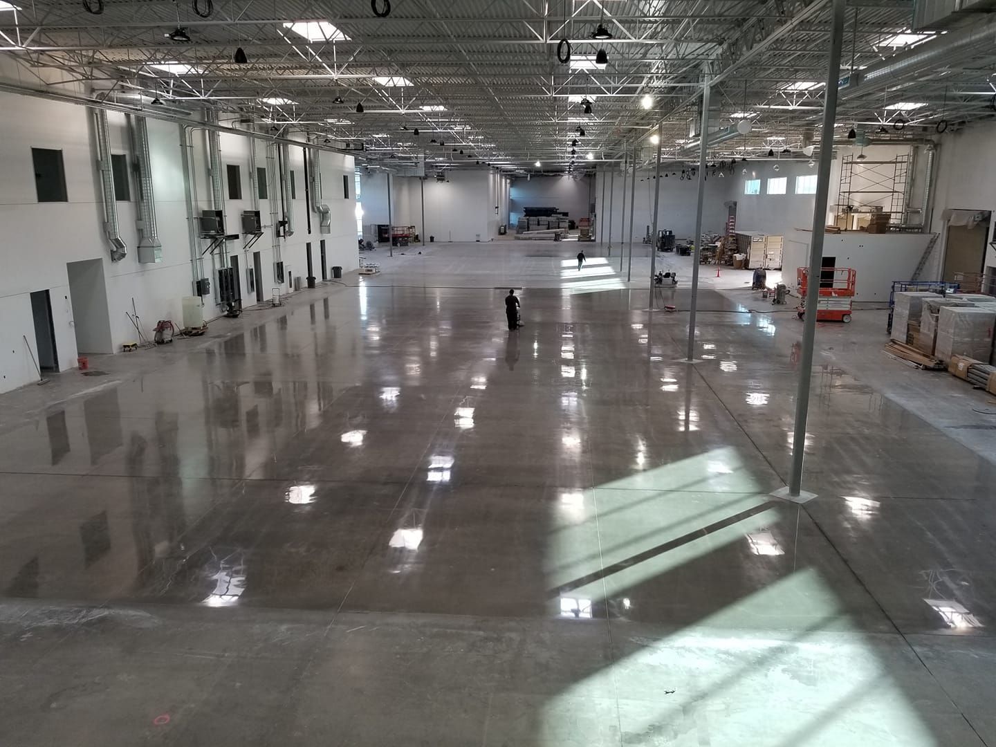 Wide, empty warehouse space with shiny concrete floor, person standing in the center.