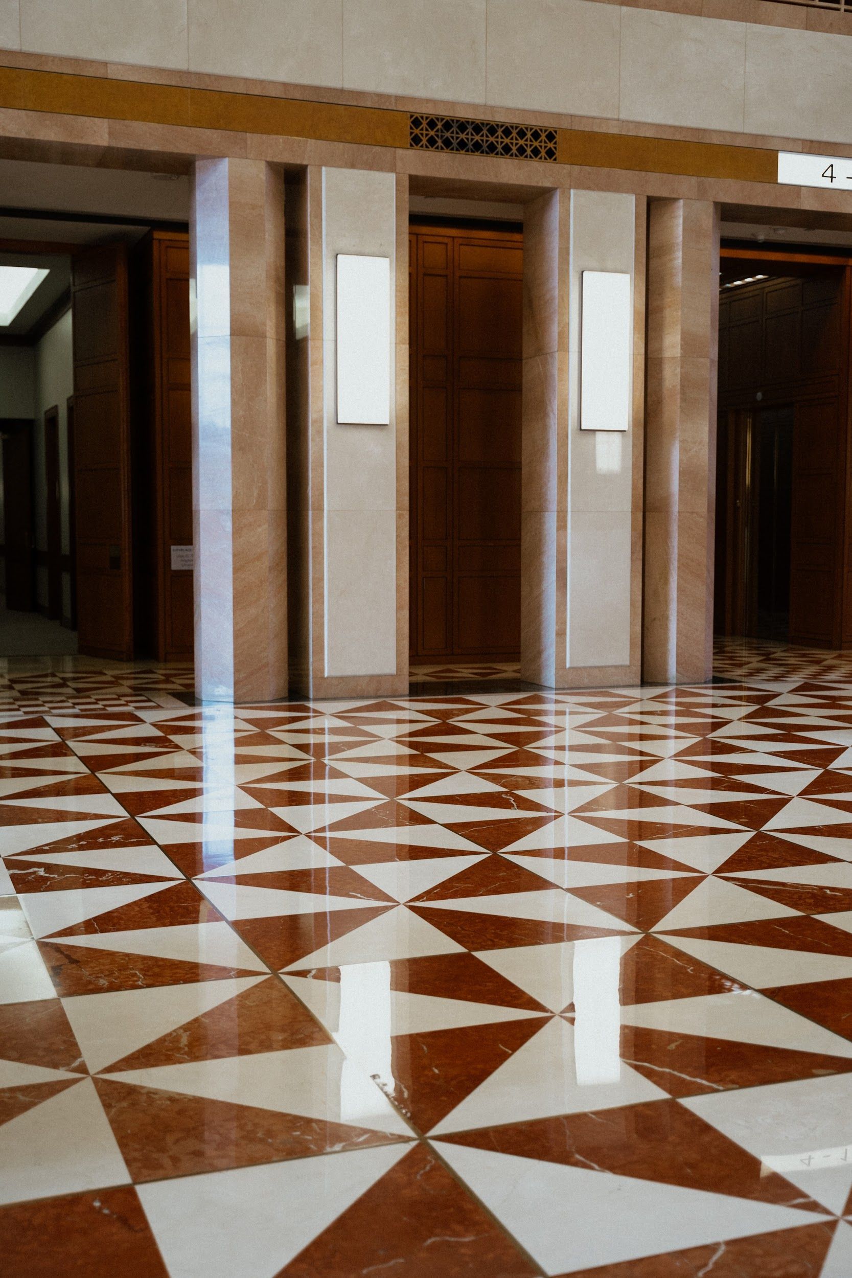 Elevator doors framed by light fixtures. Shiny red and white patterned floor in a building lobby.