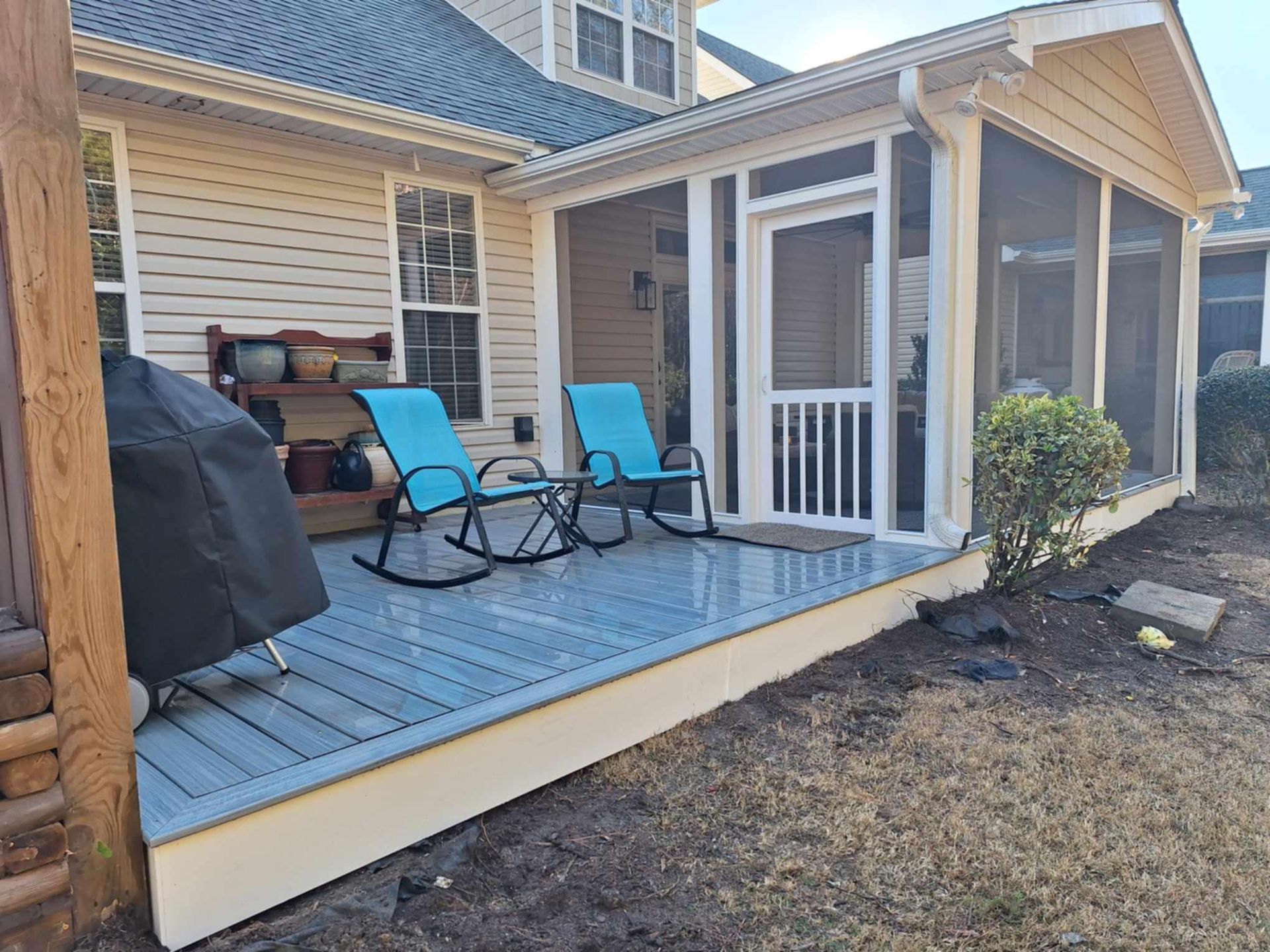 A screened in porch with two blue rocking chairs and a grill.